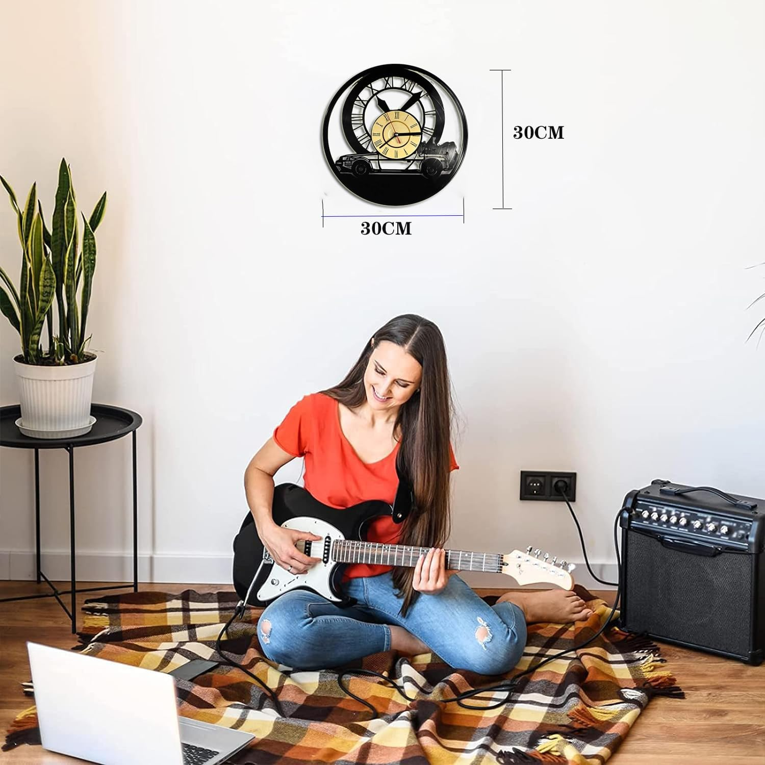 Eine Frau sitzt auf einer Decke und spielt E-Gitarre, daneben ein Verstärker und eine Uhr an der Wand.