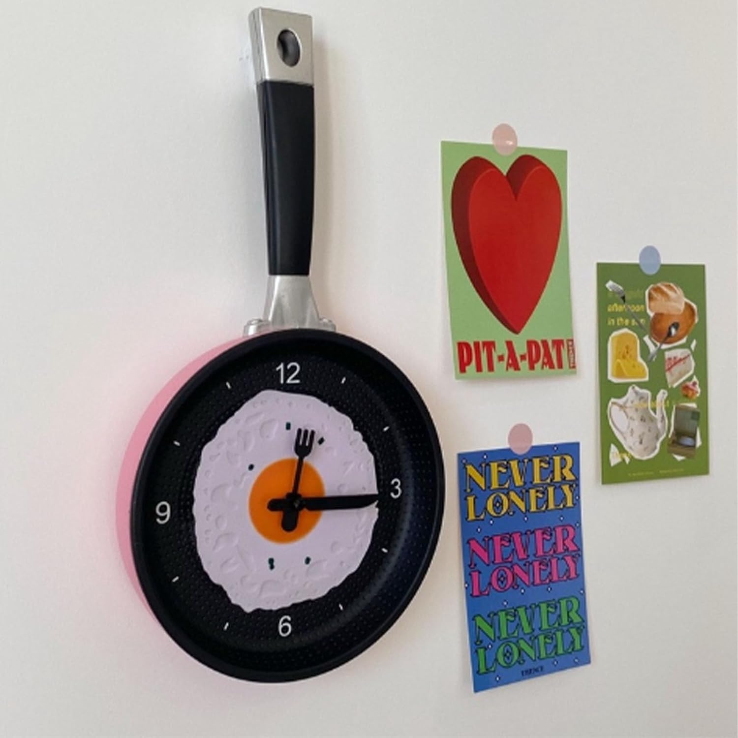 Wanduhr im Pfannendesign mit Spiegelei-Zifferblatt und drei Postkarten daneben.