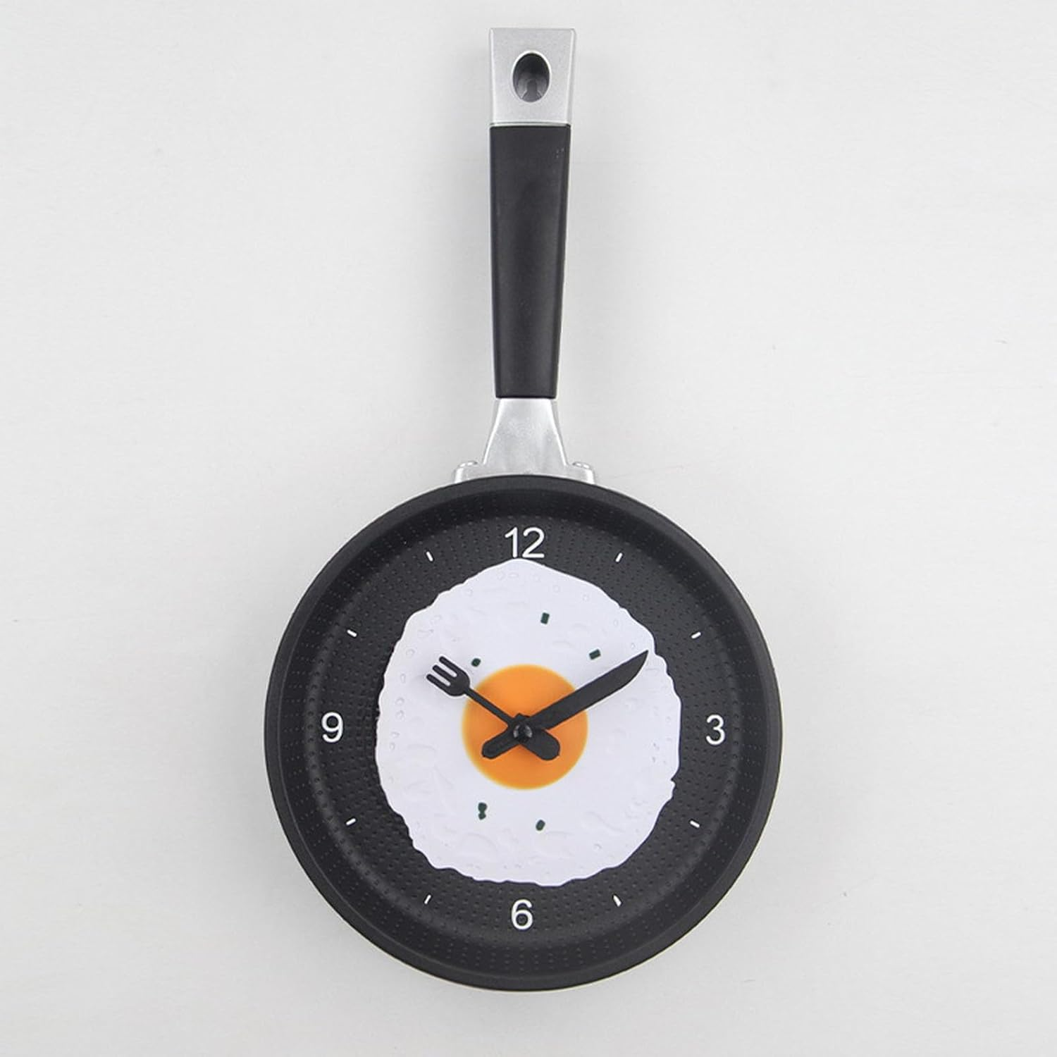 Wanduhr im Design einer schwarzen Bratpfanne mit Spiegelei, Besteckzeigern und Ziffern auf hellem Hintergrund.
