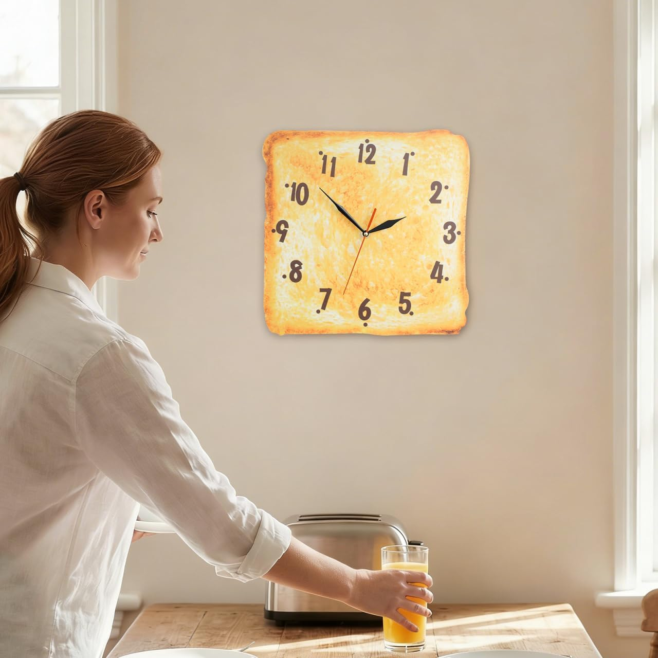 Eine Frau in weißem Hemd stellt ein Glas Orangensaft auf einen Tisch neben einem Toaster und einer Toast-Uhr.