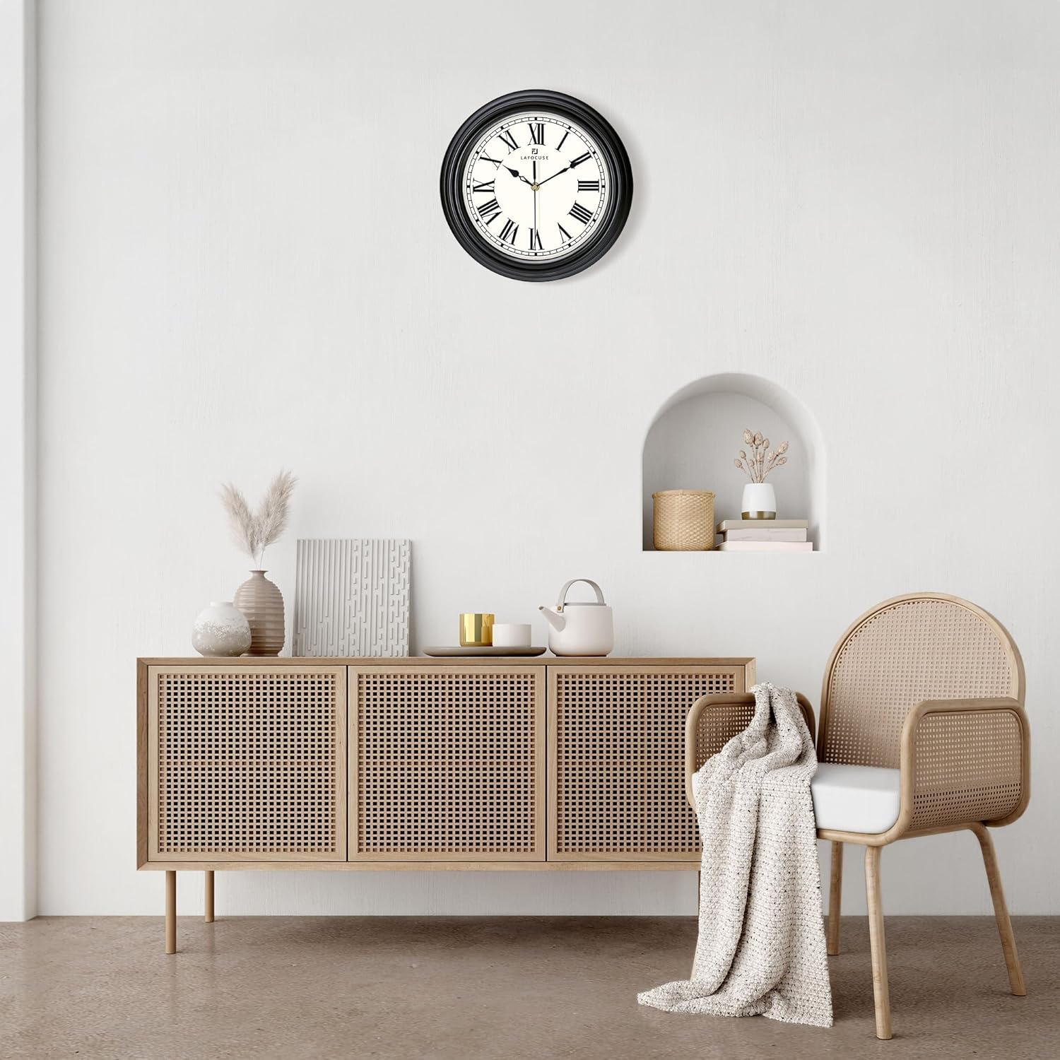 Ein minimalistischer weißer Raum mit Holzschrank, schwarzer Wanduhr und Korbstuhl mit Decke.