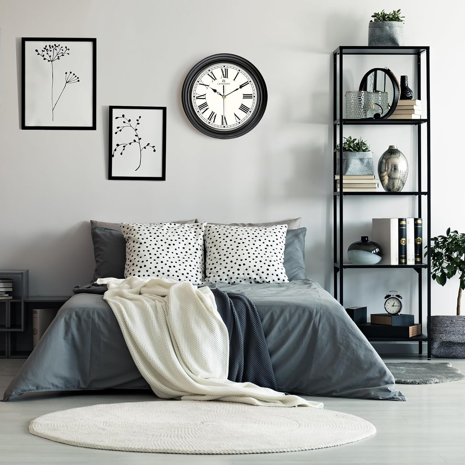 Moderne Schlafzimmereinrichtung mit grauem Bett, runder Wanduhr, Regaleinheit und Schwarz-Weiß-Postern an der Wand.