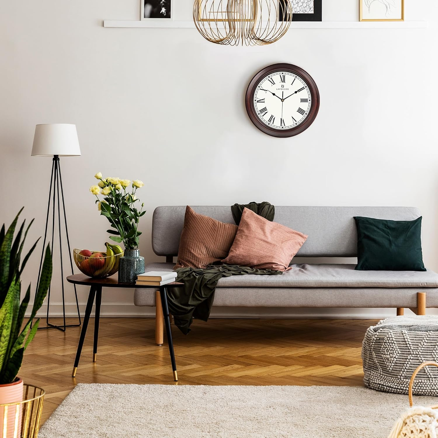 Wohnzimmer mit grauem Sofa, Kissen, runder Uhr an der Wand, Stehlampe und Kaffeetisch mit Blumen.