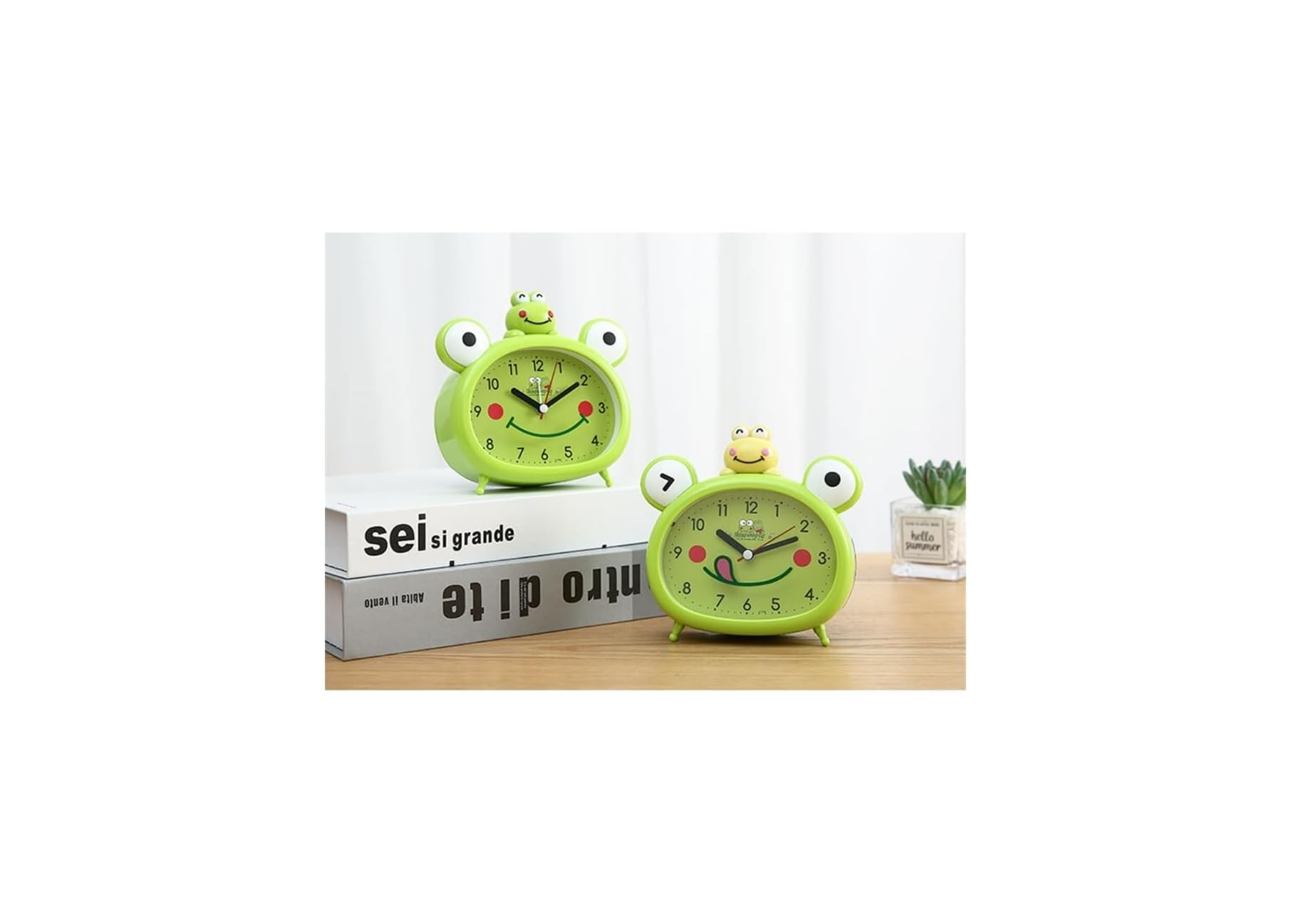 Zwei grüne Frosch-Wecker auf Büchern auf einem Holztisch, daneben eine kleine Sukkulente.