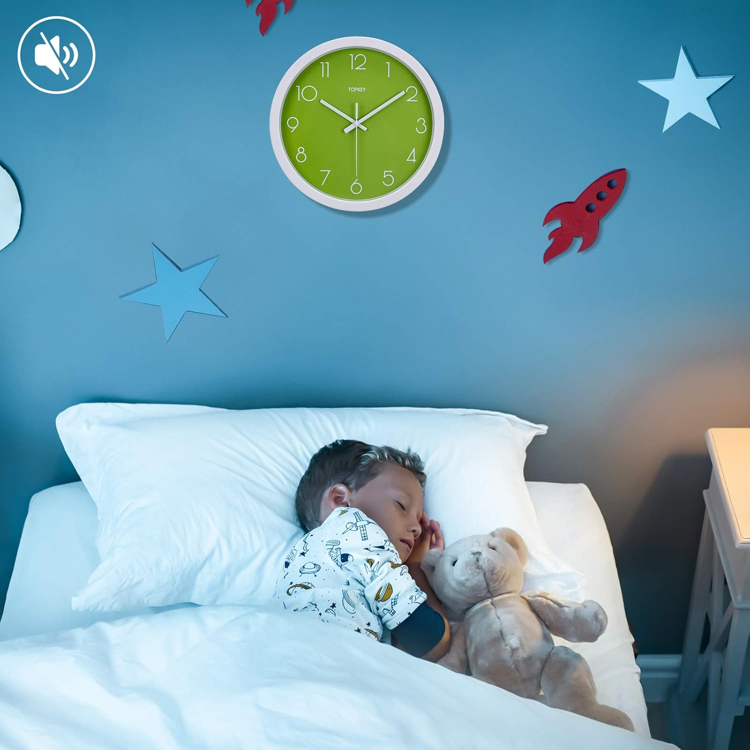 Ein Junge schläft in einem weißen Bett, umarmt einen Teddybären, unter einer blauen Wand mit grüner Uhr.