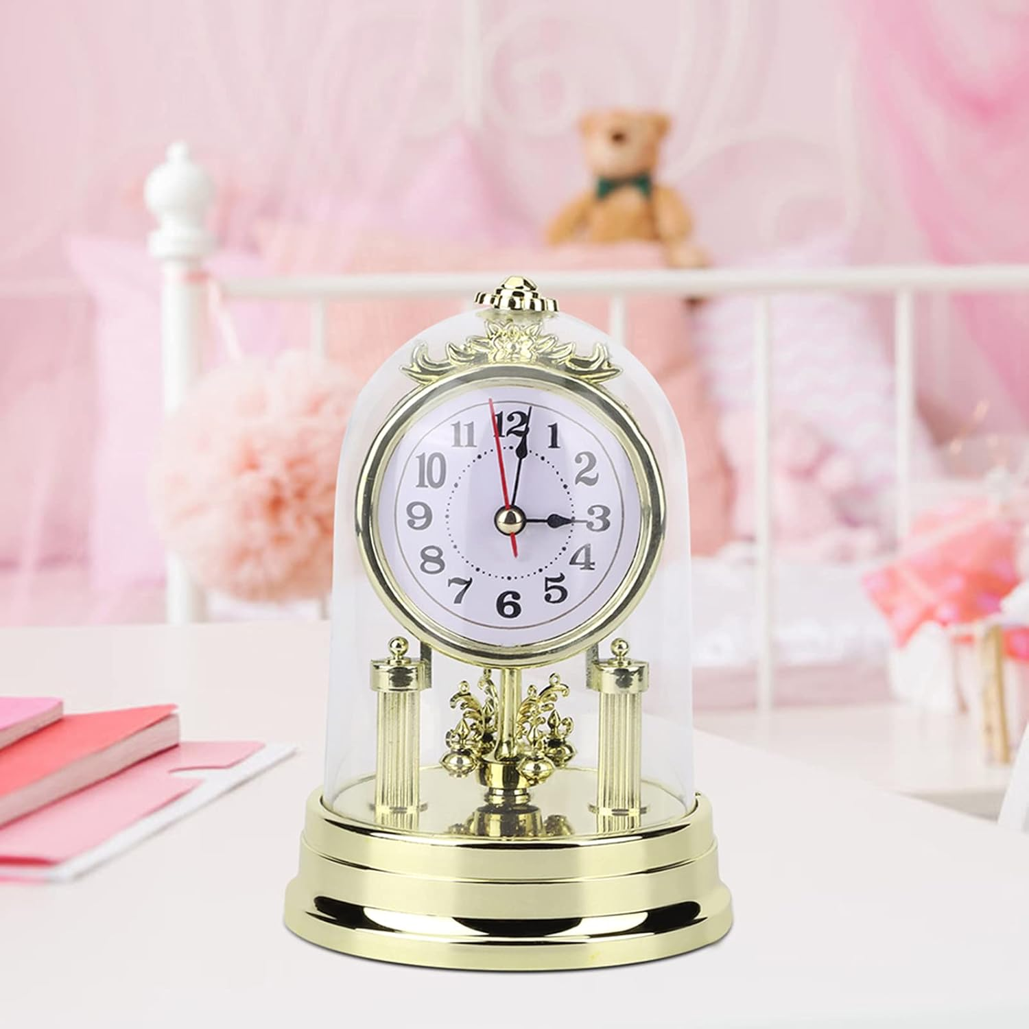 Eine goldene Standuhr unter einer Glasglocke auf einem Tisch, im Hintergrund ein rosafarbenes Kinderzimmer.