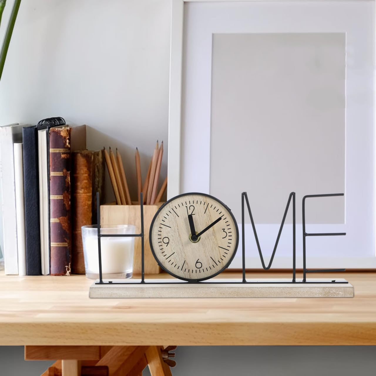Eine Schreibtischdekoration mit der Aufschrift HOME, bei der das O durch eine Uhr ersetzt ist, vor Büchern und Bilderrahmen.