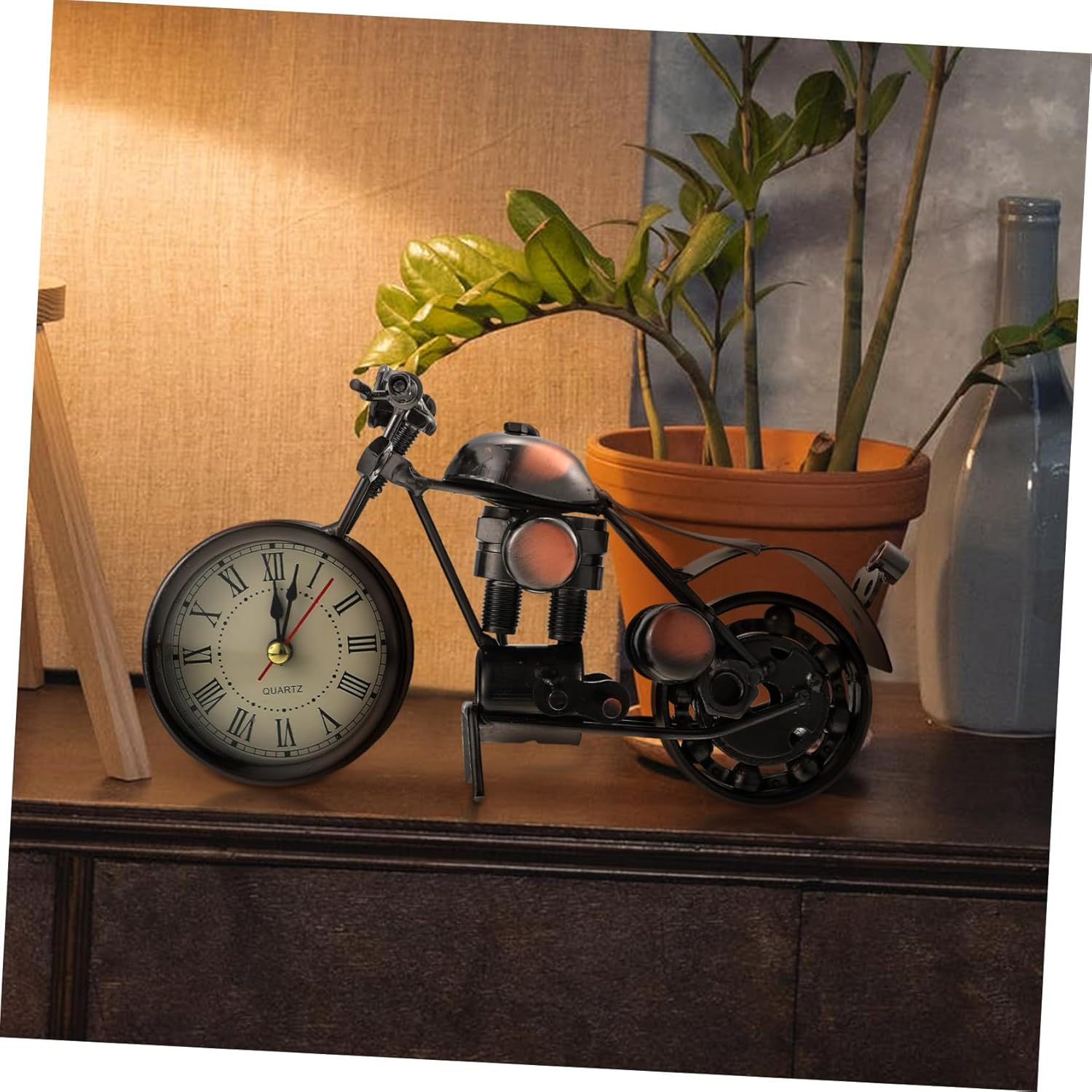 Eine Motorrad-Skulptur aus Metall mit einer Uhr als Vorderrad, dekoriert auf einem Holzschrank neben einer Pflanze.