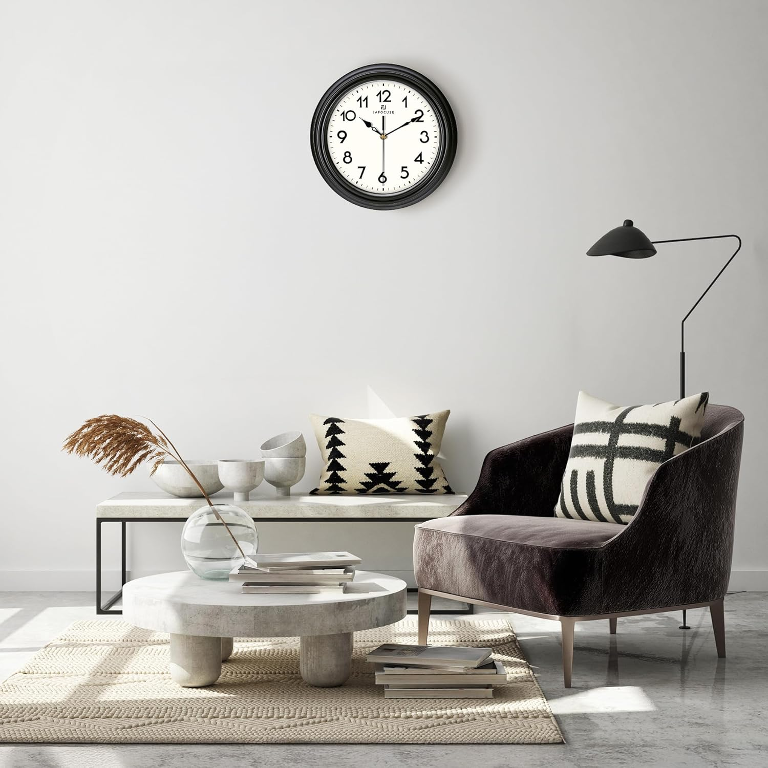 Modernes Wohnzimmer mit dunklem Sessel, weißem Tisch, Wanduhr und Stehlampe auf hellem Teppich.