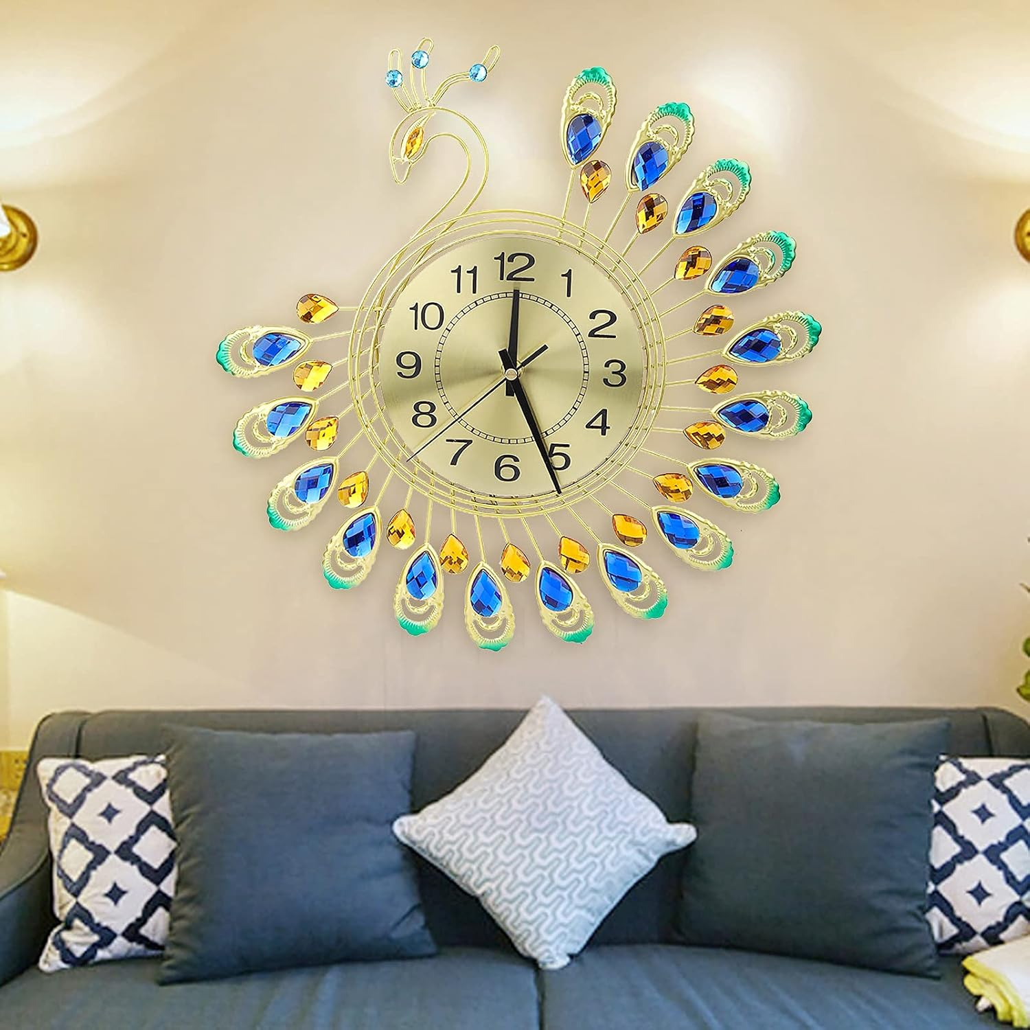 Eine goldene pfauenförmige Wanduhr mit blauen und gelben Kristallfedern hängt über einem grauen Sofa.