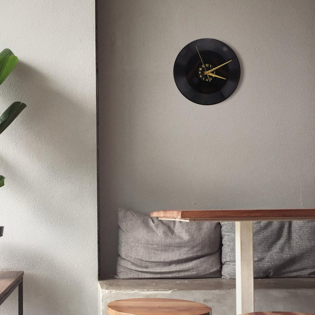 Eine schwarze Wanduhr im Schallplatten-Design hängt an einer grauen Wand über einer Sitzbank.