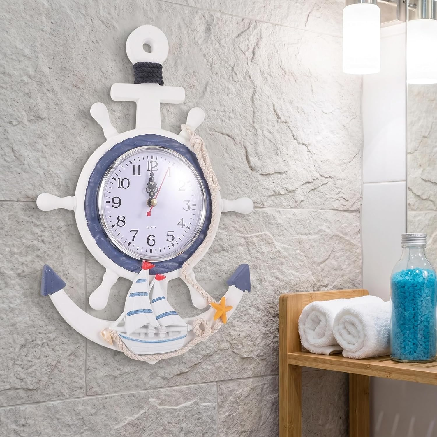 Eine marinefarbene Wanduhr mit Schiffsrad und Ankerdesign hängt an einer Steintapete im Badezimmer.