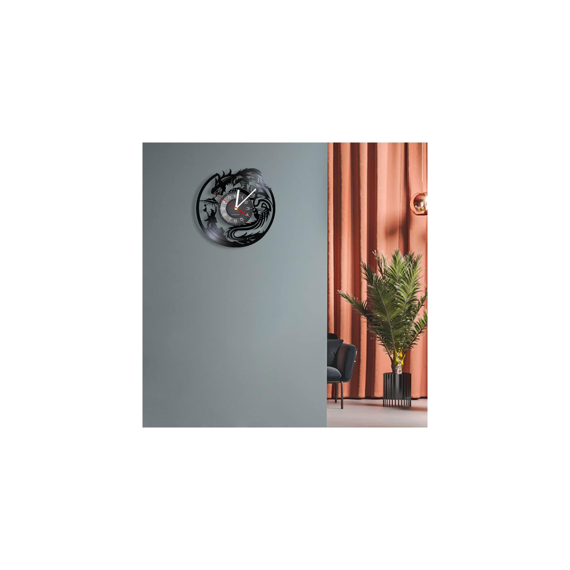 Eine schwarze Drachenwanduhr hängt an einer grauen Wand, neben einer orangefarbenen Decke und einer Pflanze.
