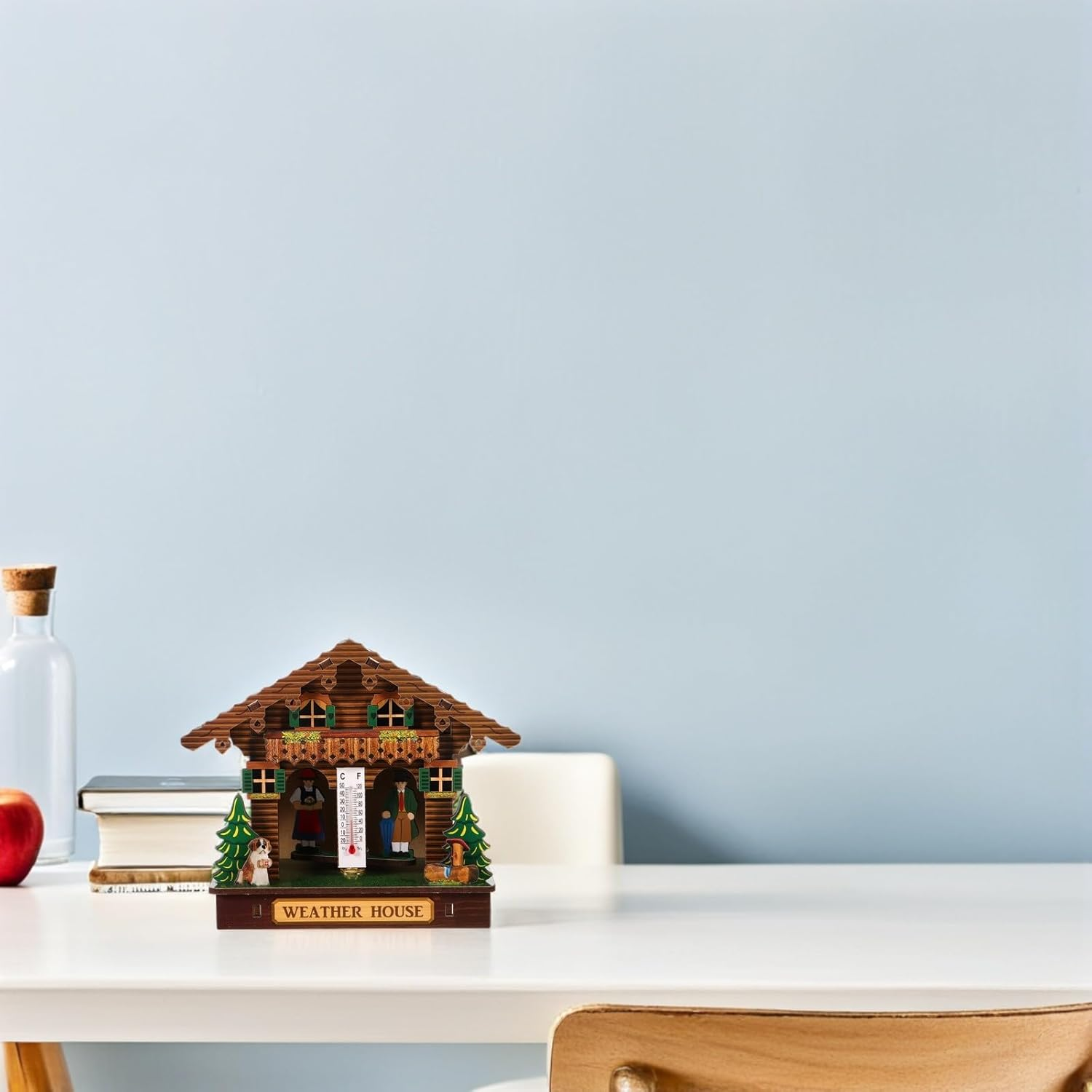 Ein hölzernes Wetterhäuschen mit Thermometer steht auf einem weißen Tisch vor einer blauen Wand.
