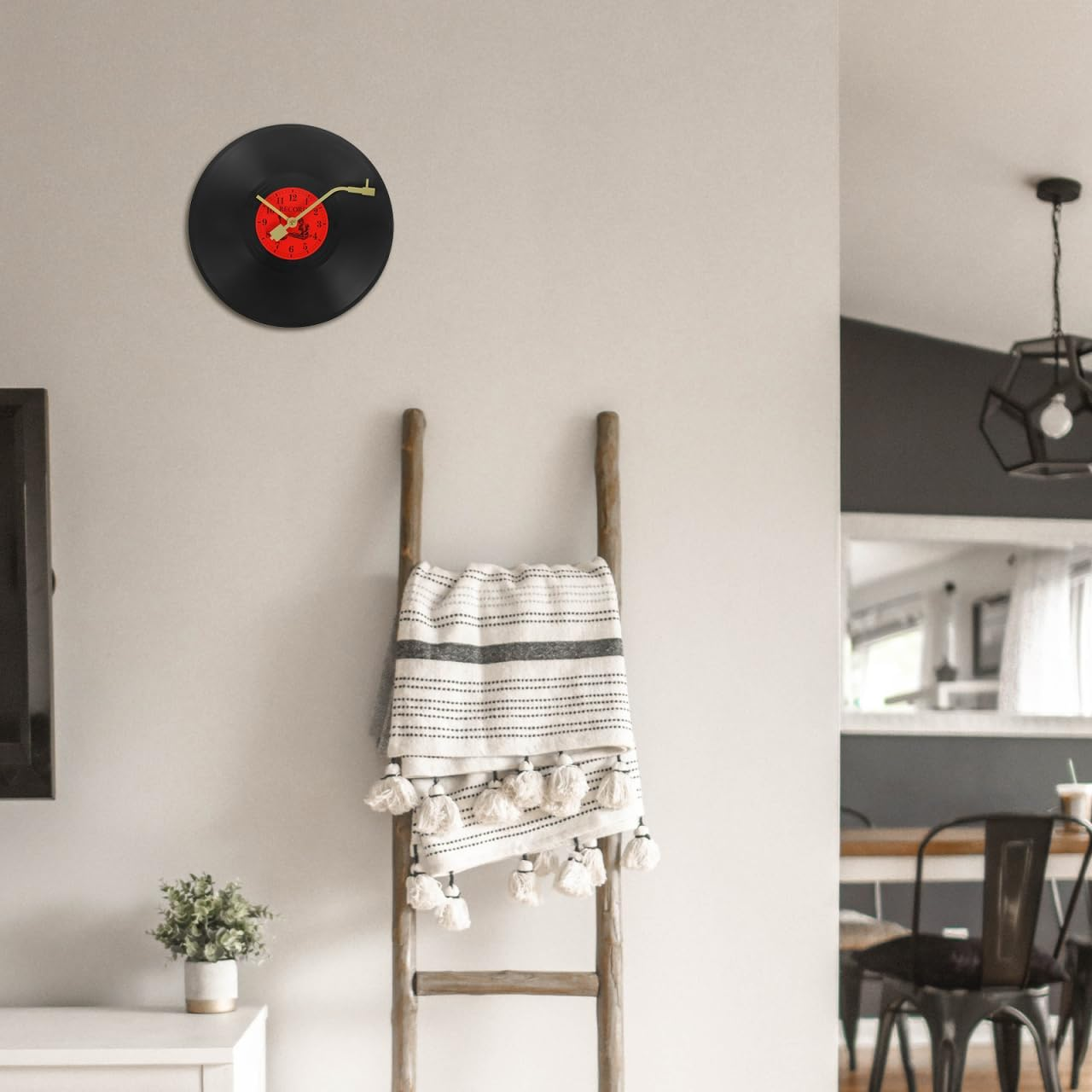 Eine Vinyl-Schallplatten-Uhr hängt an der Wand über einer Holzleiter mit Decke, ein kleiner Topf steht auf dem Schrank.