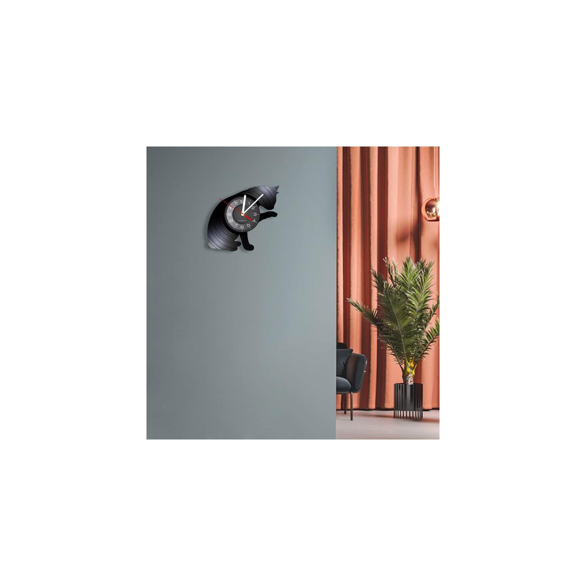 Eine schwarze Katzenuhr an einer grauen Wand, im Hintergrund ein Raum mit Vorhängen und Pflanze.