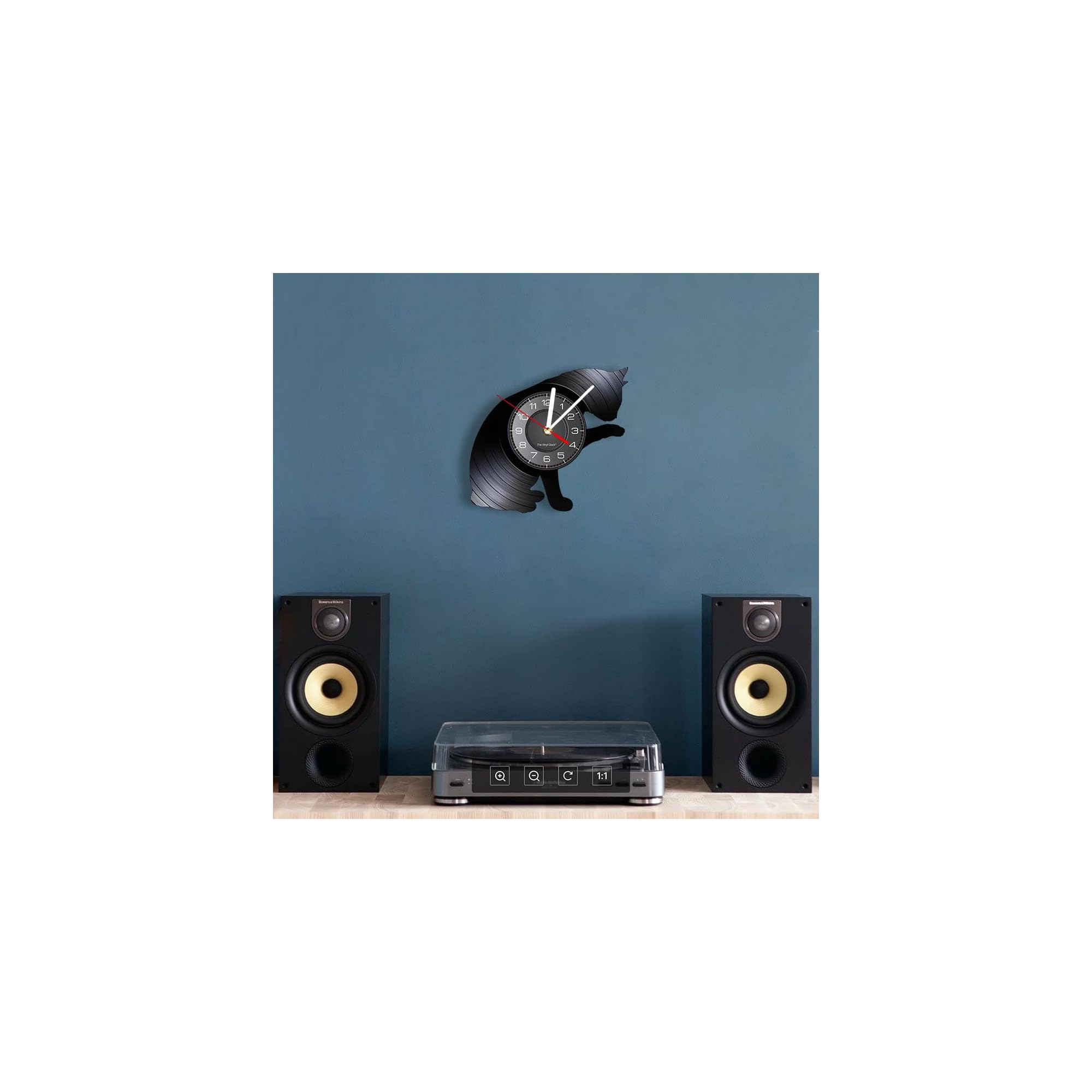 Eine Vinyluhr in Katzenform hängt über einer Stereoanlage vor einer blauen Wand.