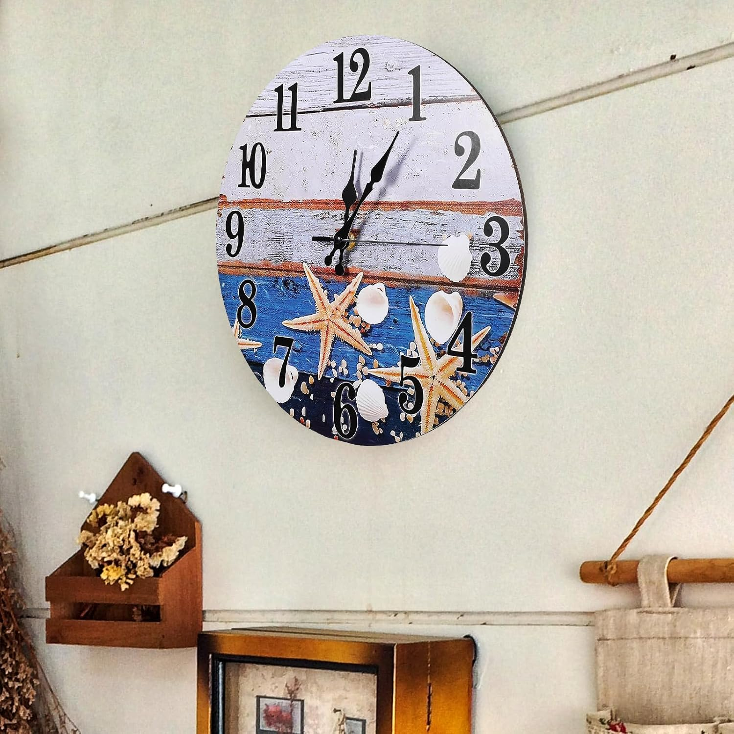 Eine runde Wanduhr mit Strandmotiv, Seesternen und Muscheln hängt an einer hellen Wand.