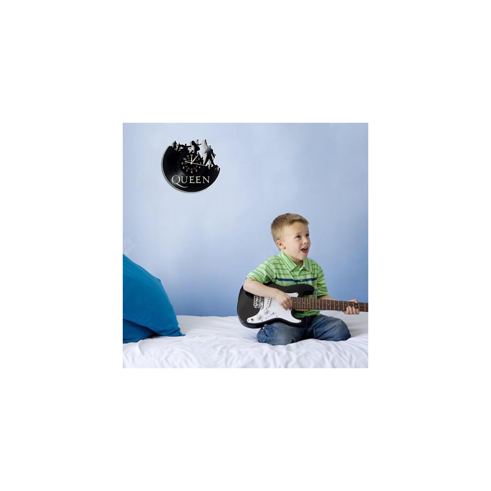 Ein Junge im gestreiften Hemd sitzt auf einem Bett und spielt eine kleine E-Gitarre, an der Wand hängt eine Queen-Uhr.