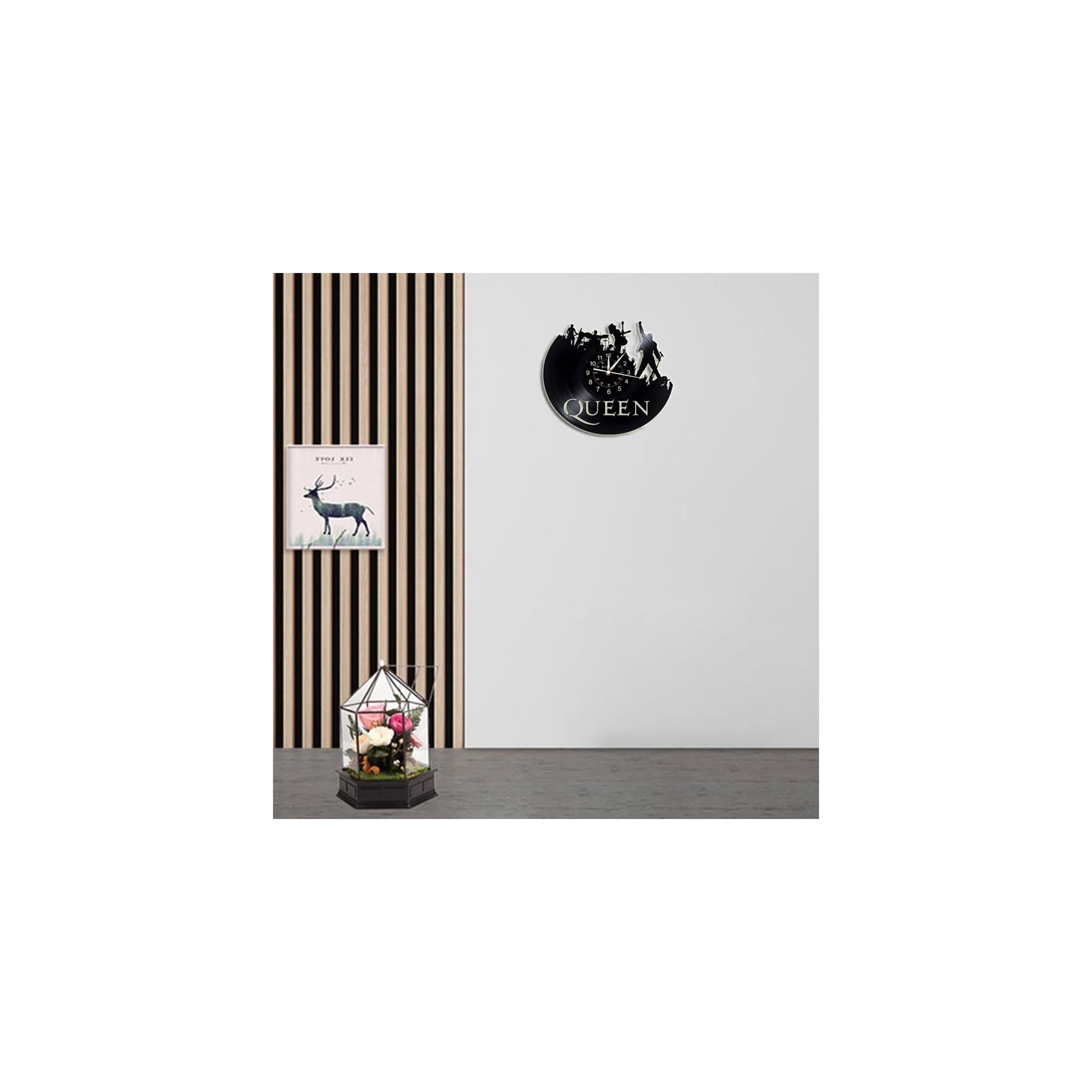 Eine Queen-Schallplattenuhr hängt an einer weißen Wand neben Holzpaneelen, ein kleines Blumenarrangement steht unten.