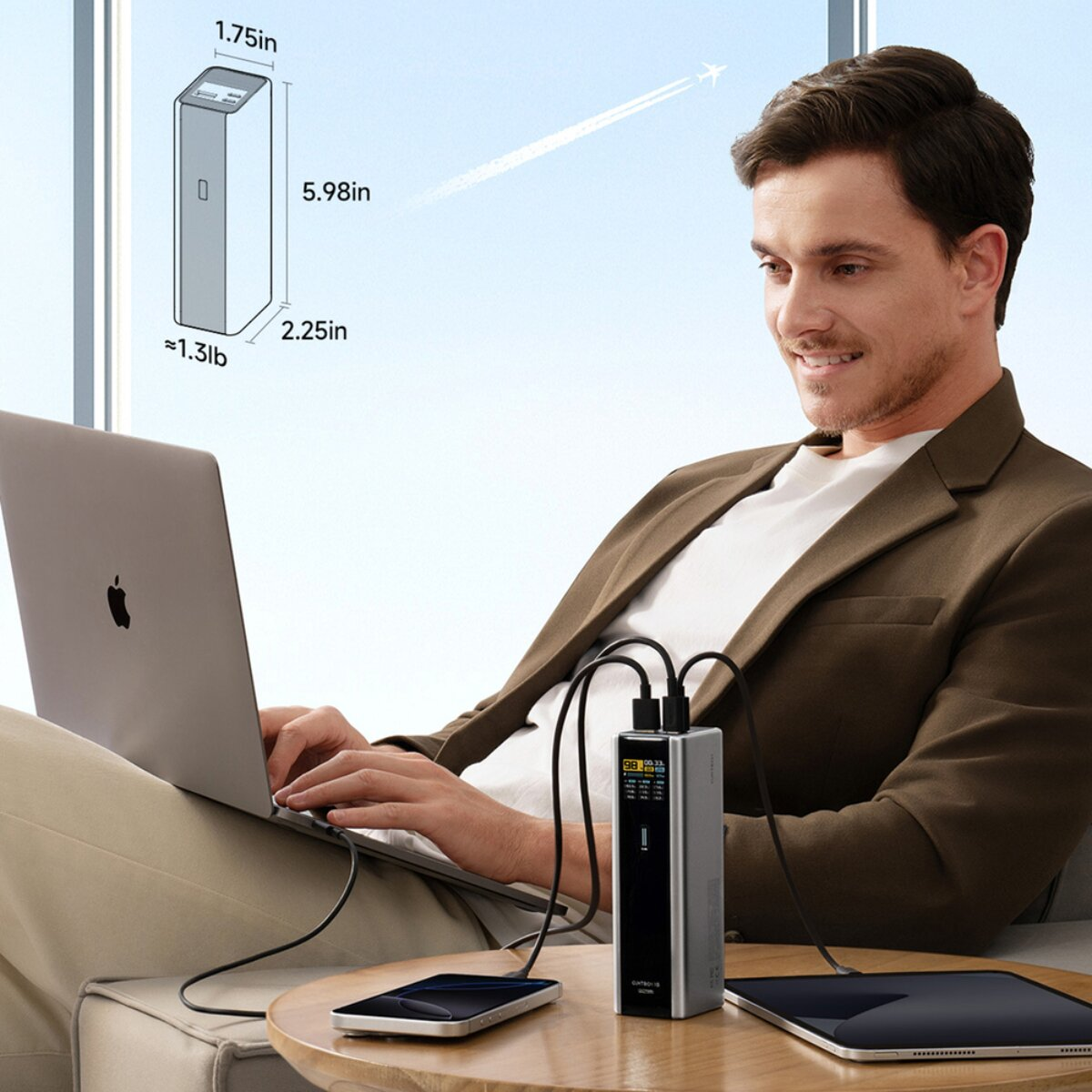 Mann arbeitet am Laptop, während eine Powerbank Laptop, Handy und Tablet lädt.
