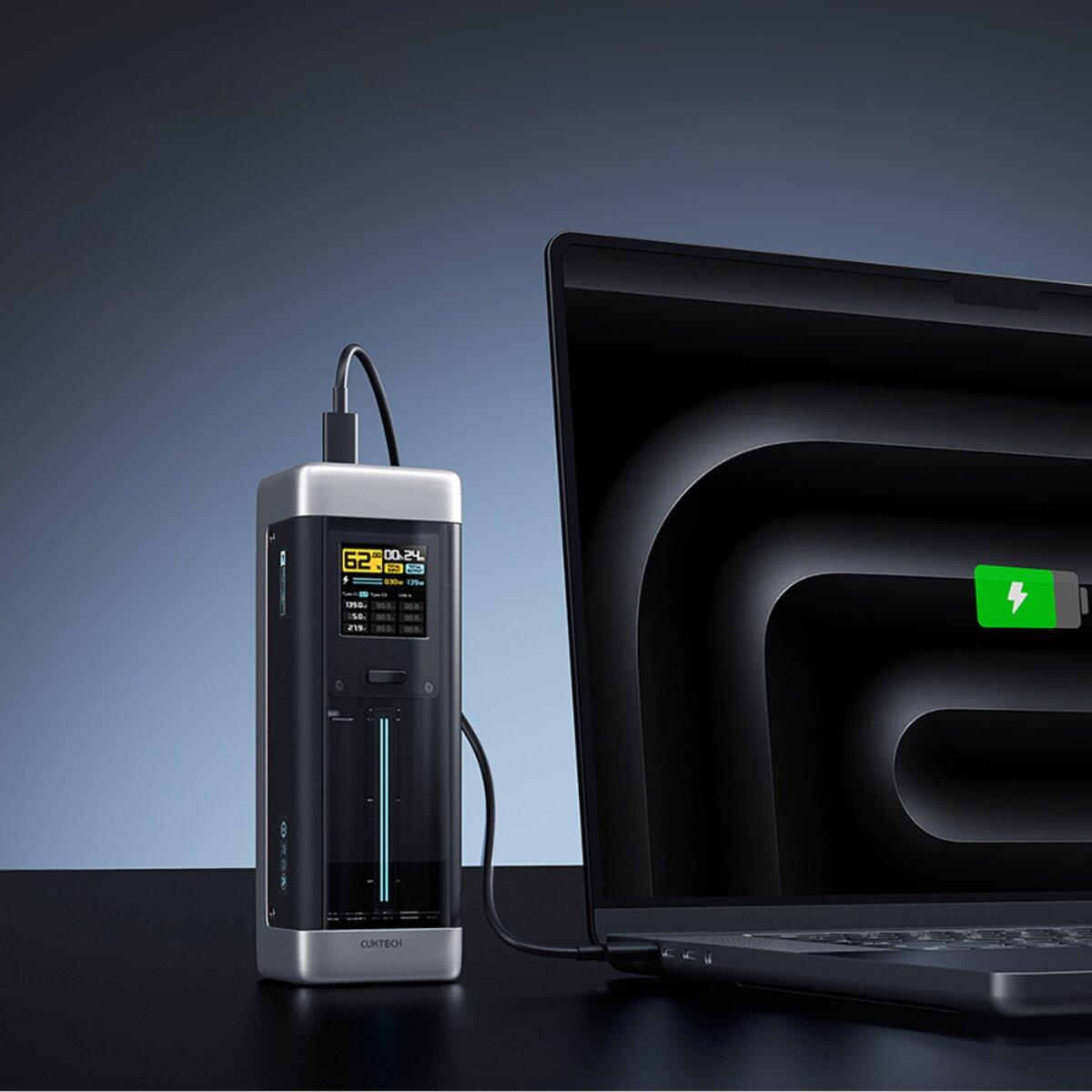 Un power bank portatile con display carica un laptop, entrambi su una superficie nera.