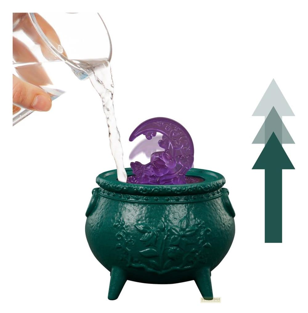 Wasser wird aus einem Glas in einen grünen Kessel mit einer lilafarbenen Mondfigur und aufsteigenden Pfeilen gegossen.
