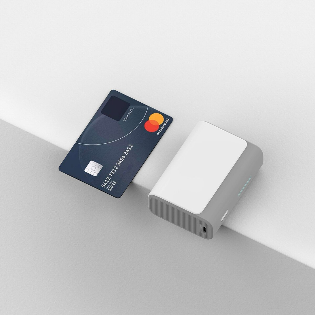 Eine dunkelblaue Mastercard und ein weißes Lesegerät liegen auf einer minimalistischen weißen Fläche.