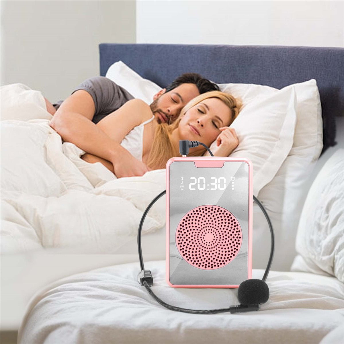 Ein rosafarbener Sprachverstärker mit Mikrofon steht auf dem Bett, während im Hintergrund ein Paar schläft.