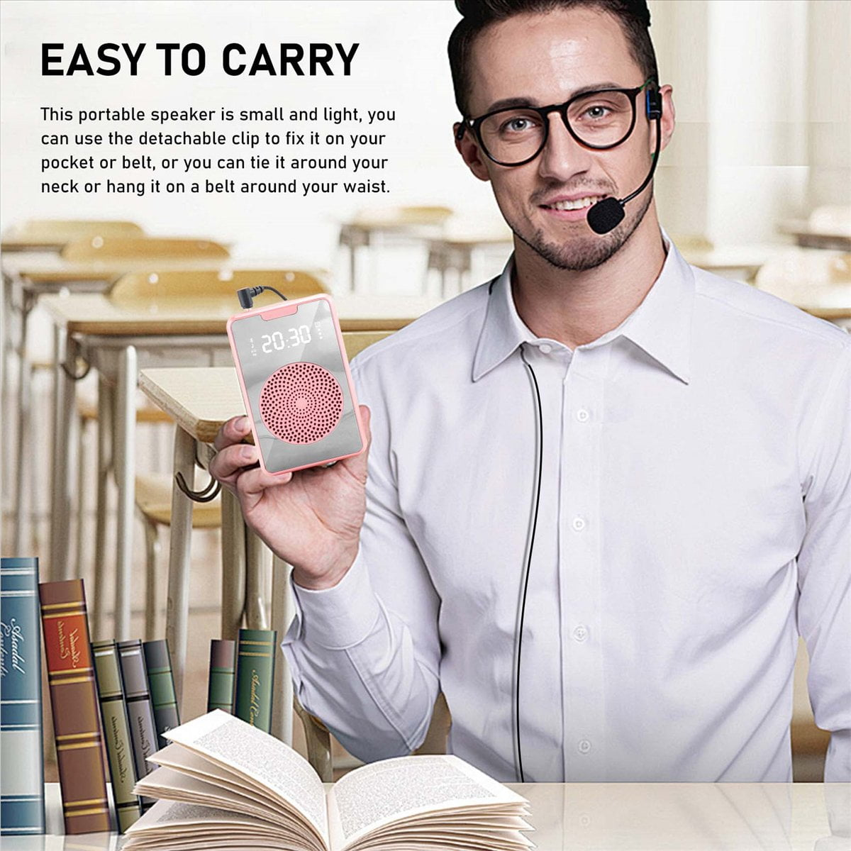 Ein Mann mit Brille und Mikrofon hält einen rosafarbenen tragbaren Lautsprecher in einem Klassenzimmer.