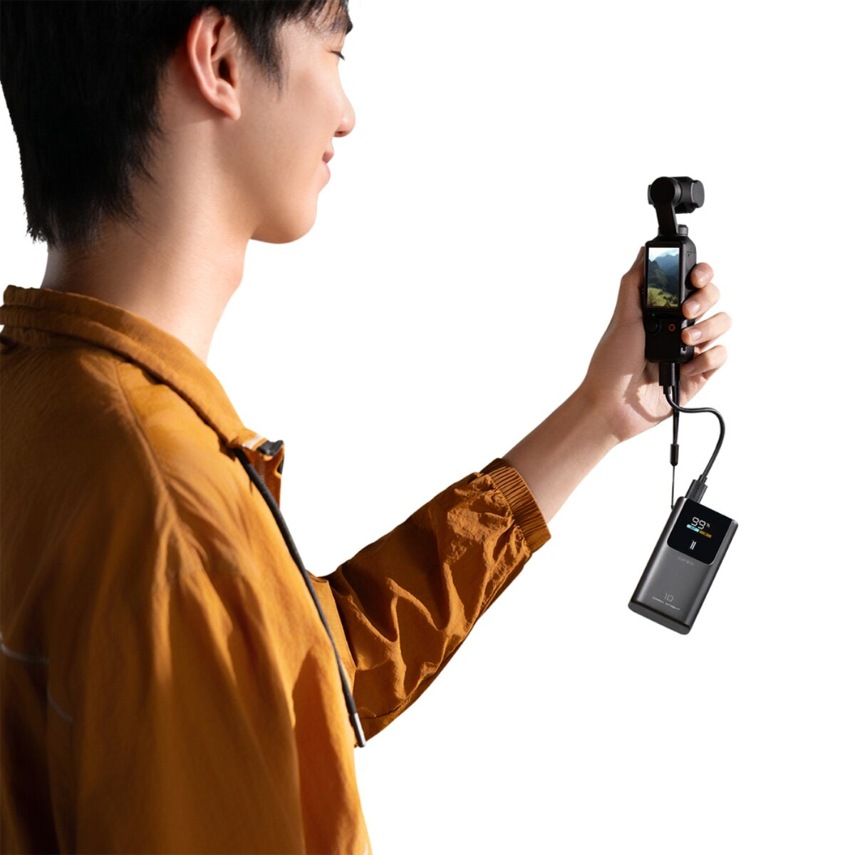 Ein junger Mann im gelben Hemd hält eine kleine Gimbal-Kamera mit Powerbank vor weißem Hintergrund.