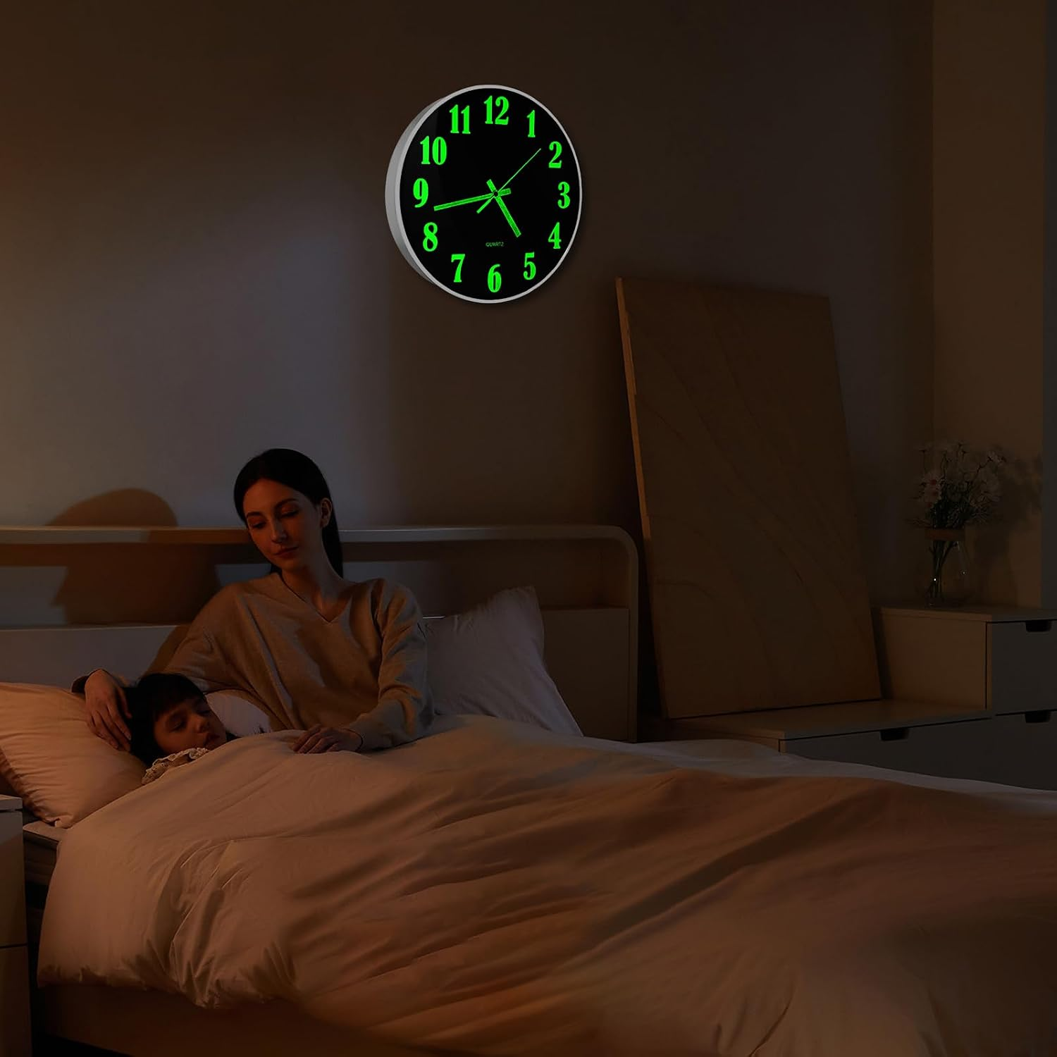 Eine Frau sitzt nachts am Bett eines schlafenden Kindes, während an der Wand eine grün leuchtende Uhr hängt.
