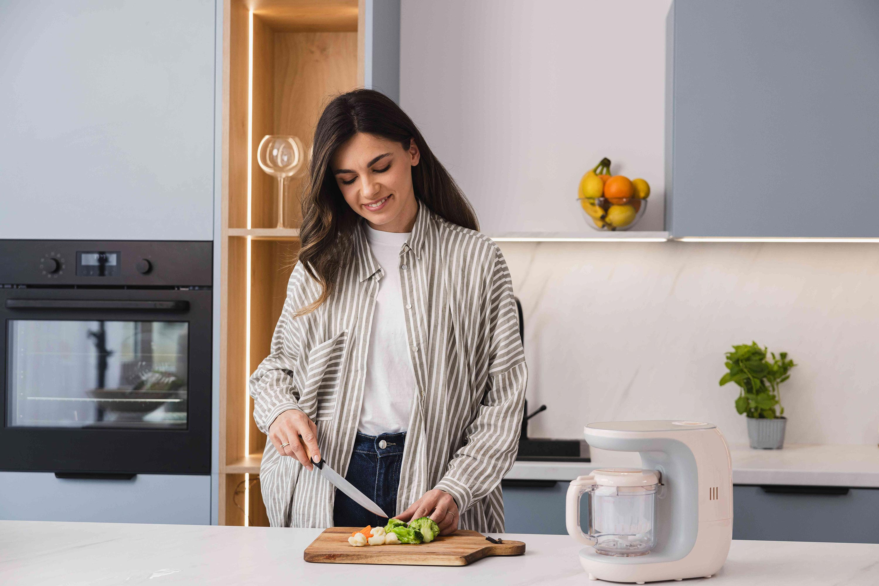 Una donna in una cucina moderna taglia le verdure su un tagliere di legno.