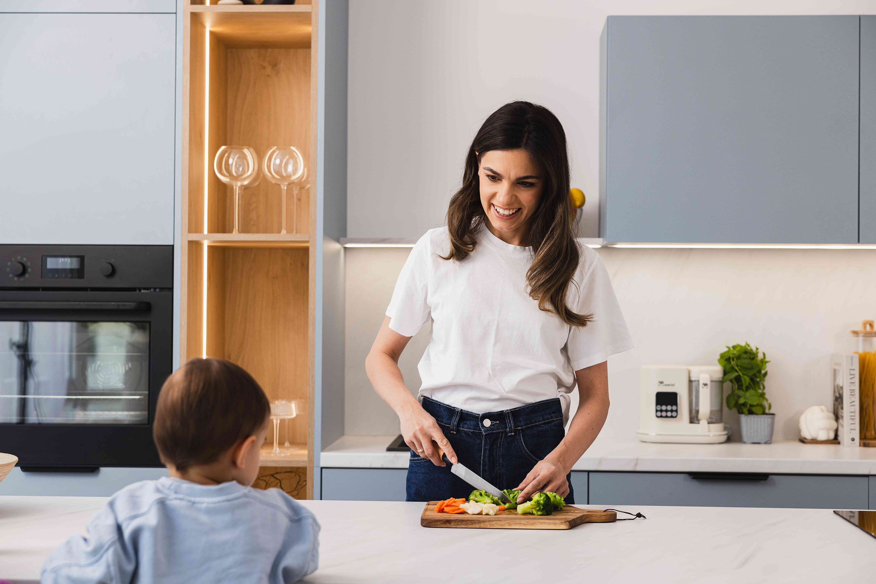 Una donna taglia verdure in una cucina moderna mentre un bambino guarda.