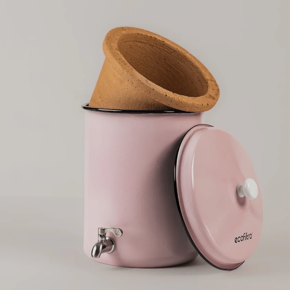 Un filtro per acqua rosa con inserto in argilla, rubinetto in metallo e coperchio aperto.