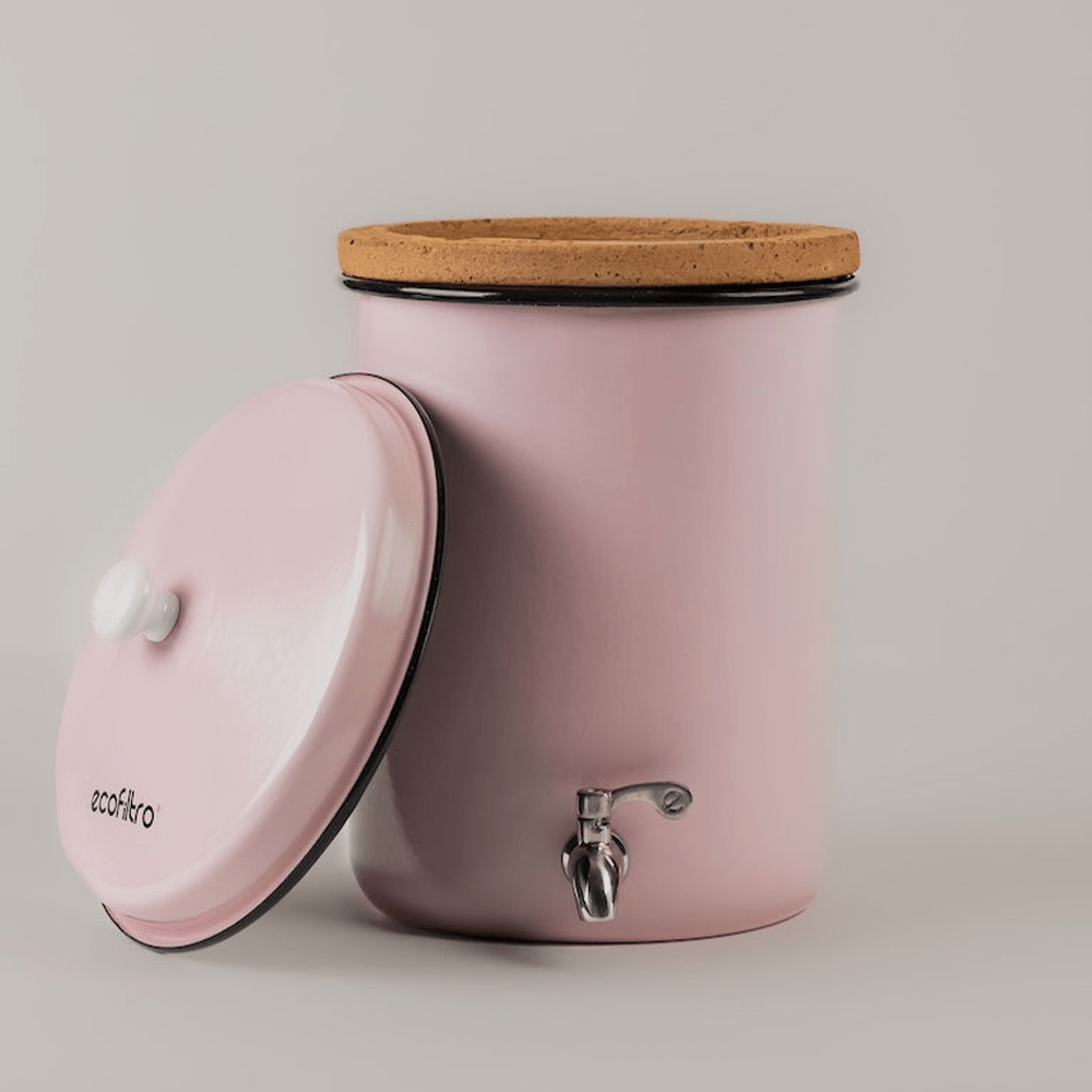 Un distributore d'acqua in metallo rosa con rubinetto argentato, bordo in sughero e coperchio rosa.