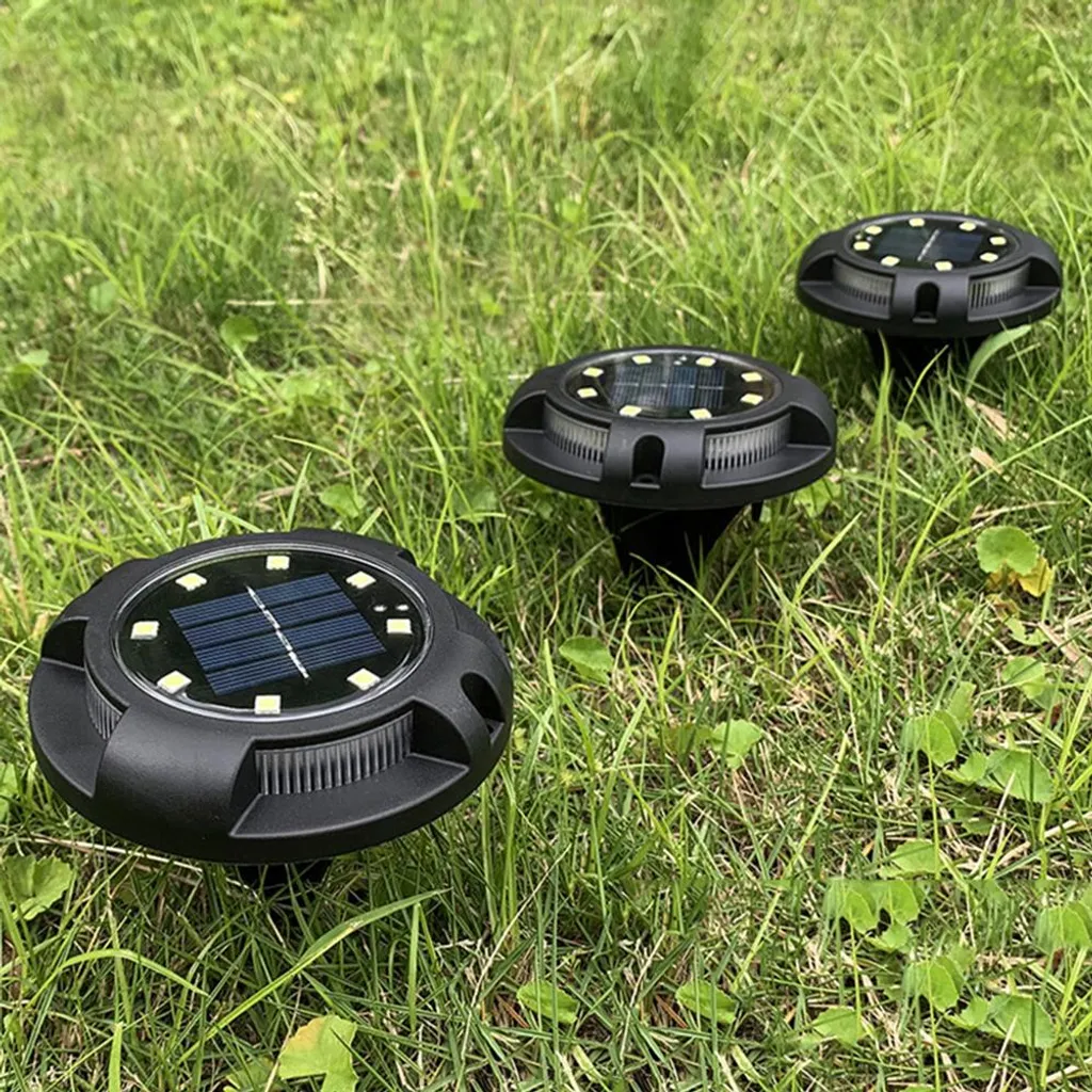 Drei runde, schwarze Solargartenleuchten sind in saftig grünes Gras eingebettet.