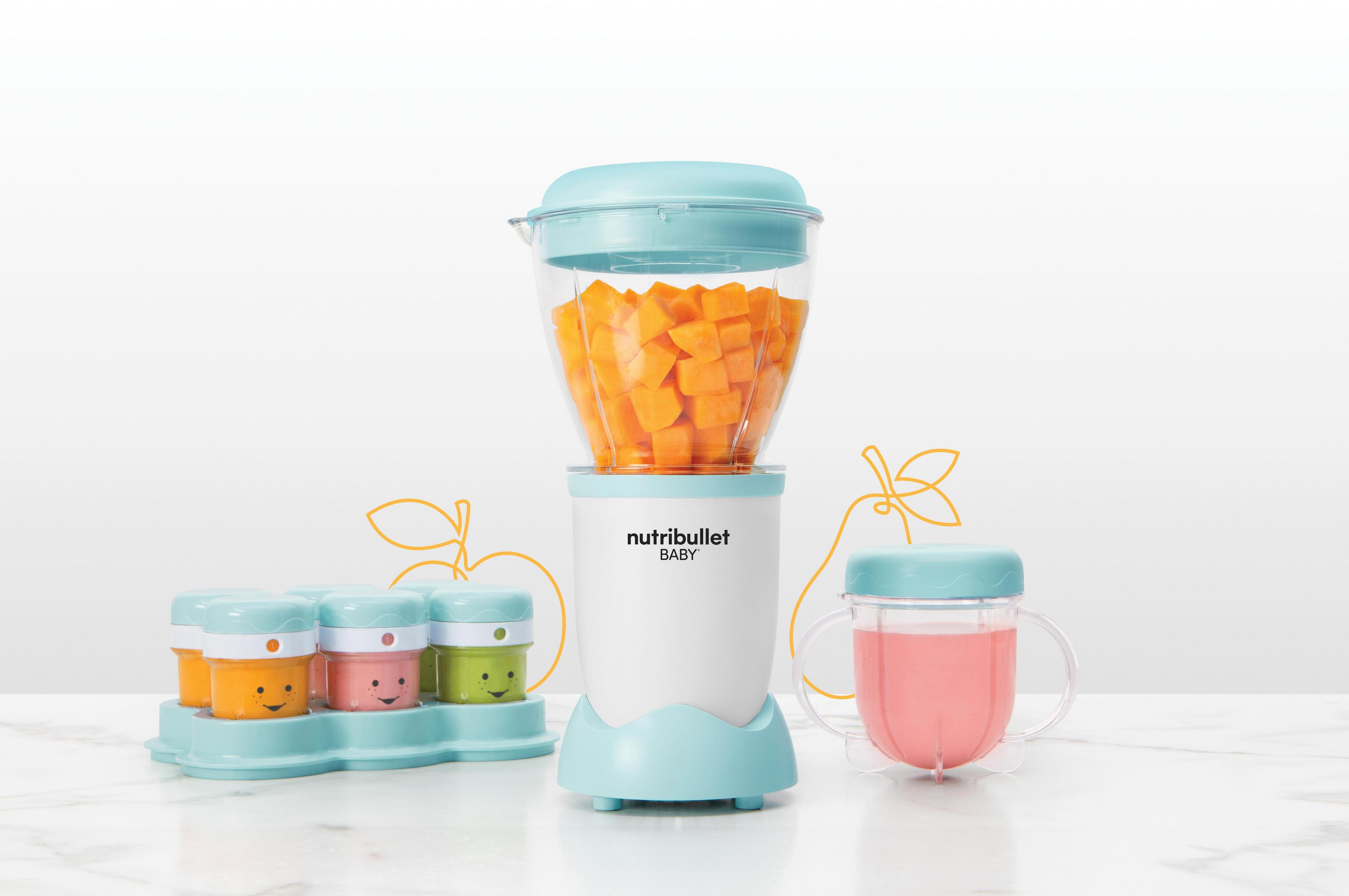Un frullatore Nutribullet Baby con verdure arancioni, piccoli contenitori e una tazza rosa su superficie bianca.