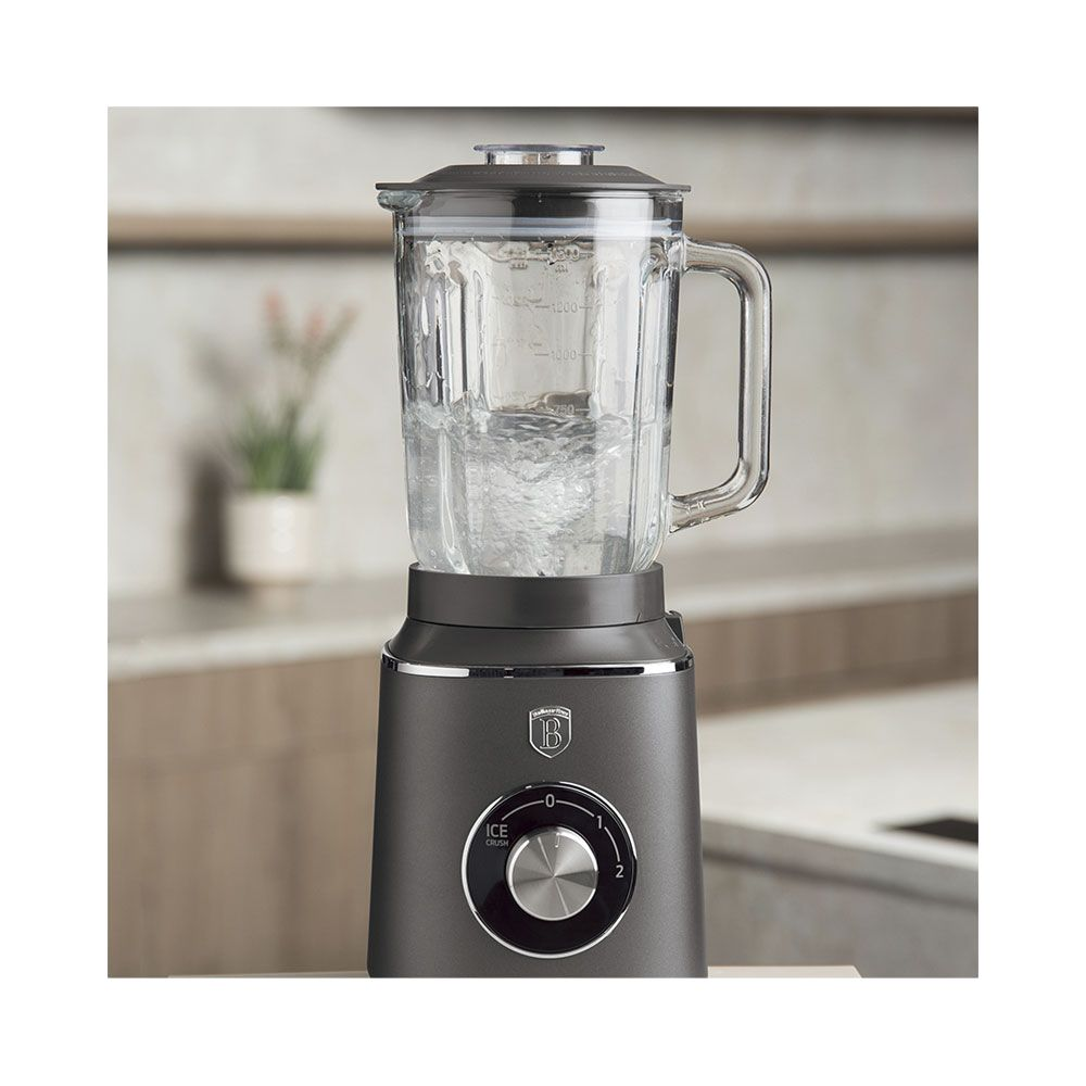 Un frullatore grigio da cucina con caraffa in vetro su un ripiano.
