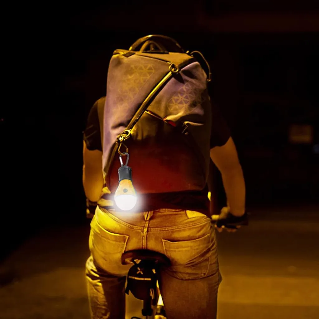 Ein Radfahrer mit Rucksack fährt im Dunkeln, beleuchtet von einer leuchtenden Glühbirne.
