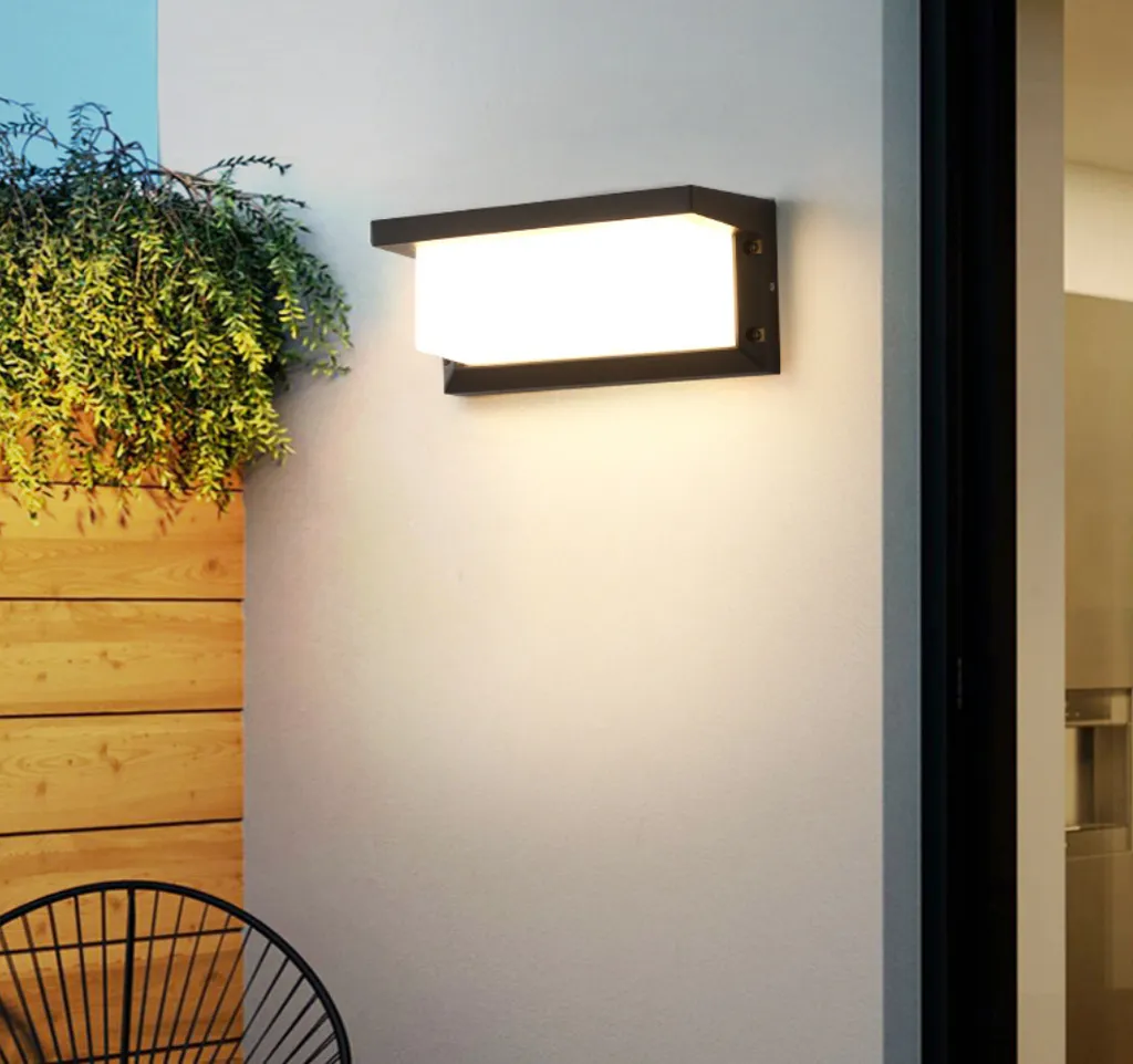 Eine schwarze Außenwandleuchte leuchtet warm an einer hellen Wand neben Holzvertäfelung und Pflanzen.