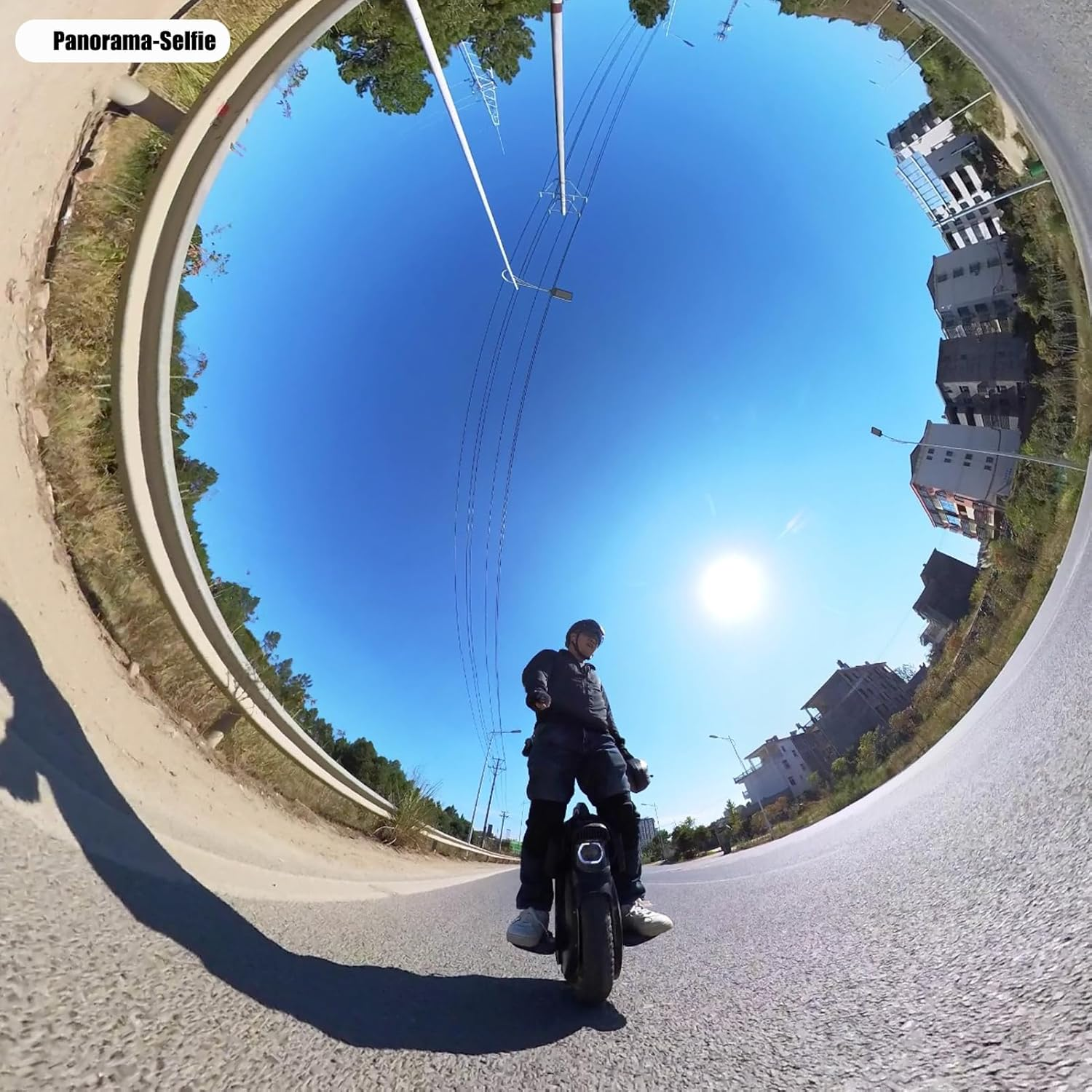 Fisheye-Selfie einer Person auf einem Einrad auf einer sonnigen Straße, umgeben von Gebäuden und Masten unter blauem Himmel.