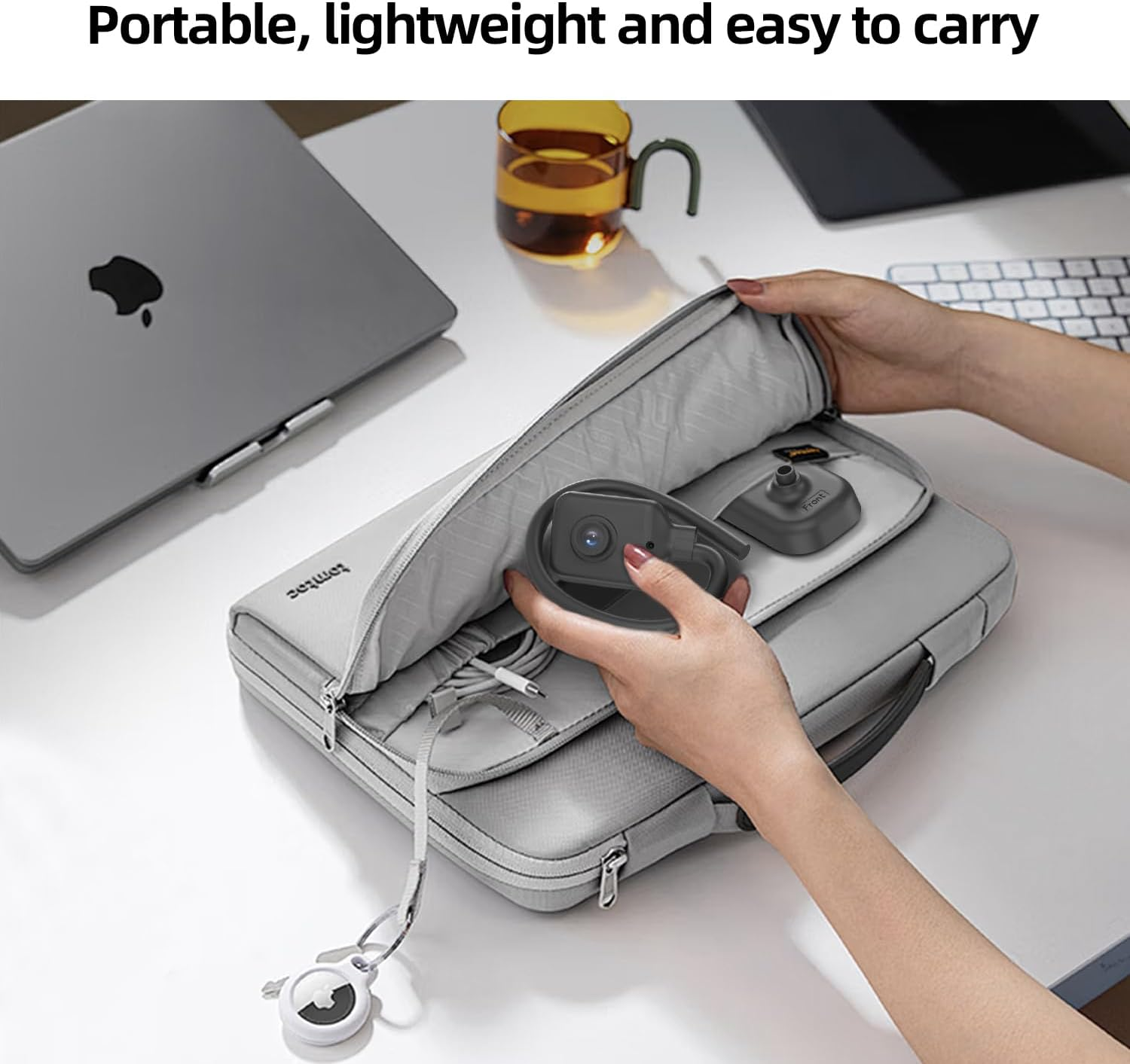 Jemand nimmt eine kleine Kamera aus einer grauen Laptoptasche auf einem Schreibtisch.