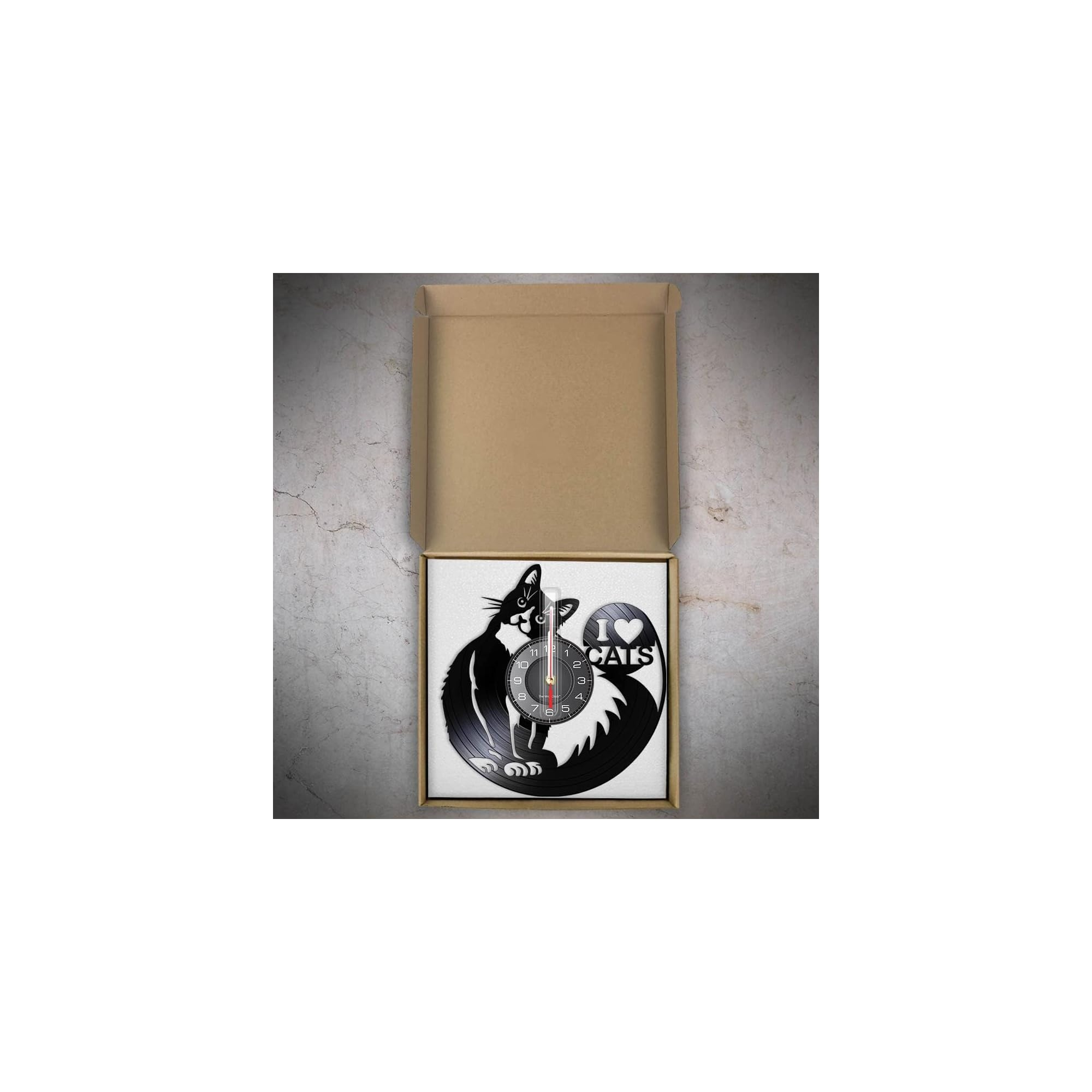 Eine schwarze Vinyl-Wanduhr mit Katzen-Motiv in einem offenen Karton auf grauem Untergrund.