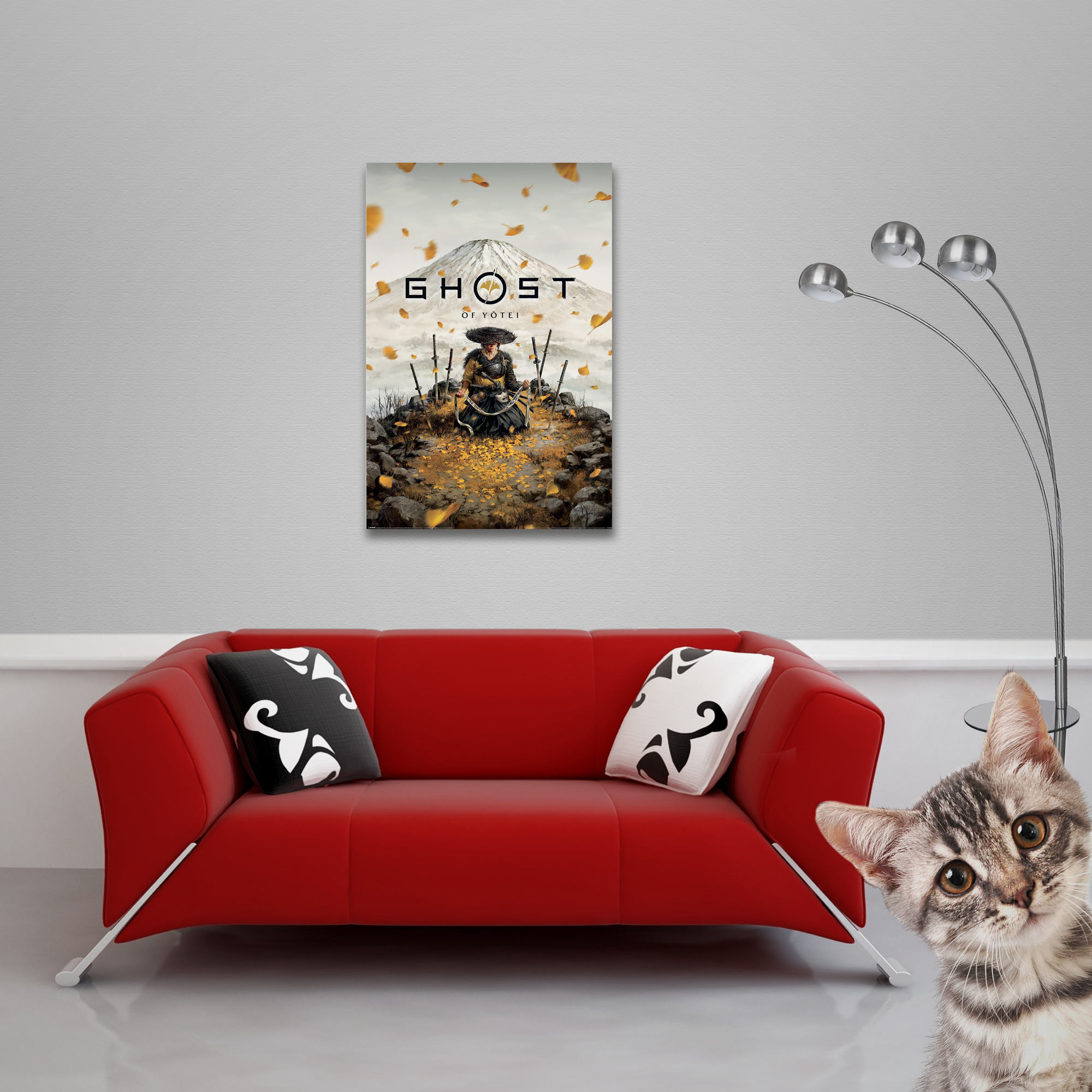 Ein rotes Sofa mit Kissen steht vor einer grauen Wand mit Plakat; rechts peppt eine Katze hervor und eine Lampe steht daneben.