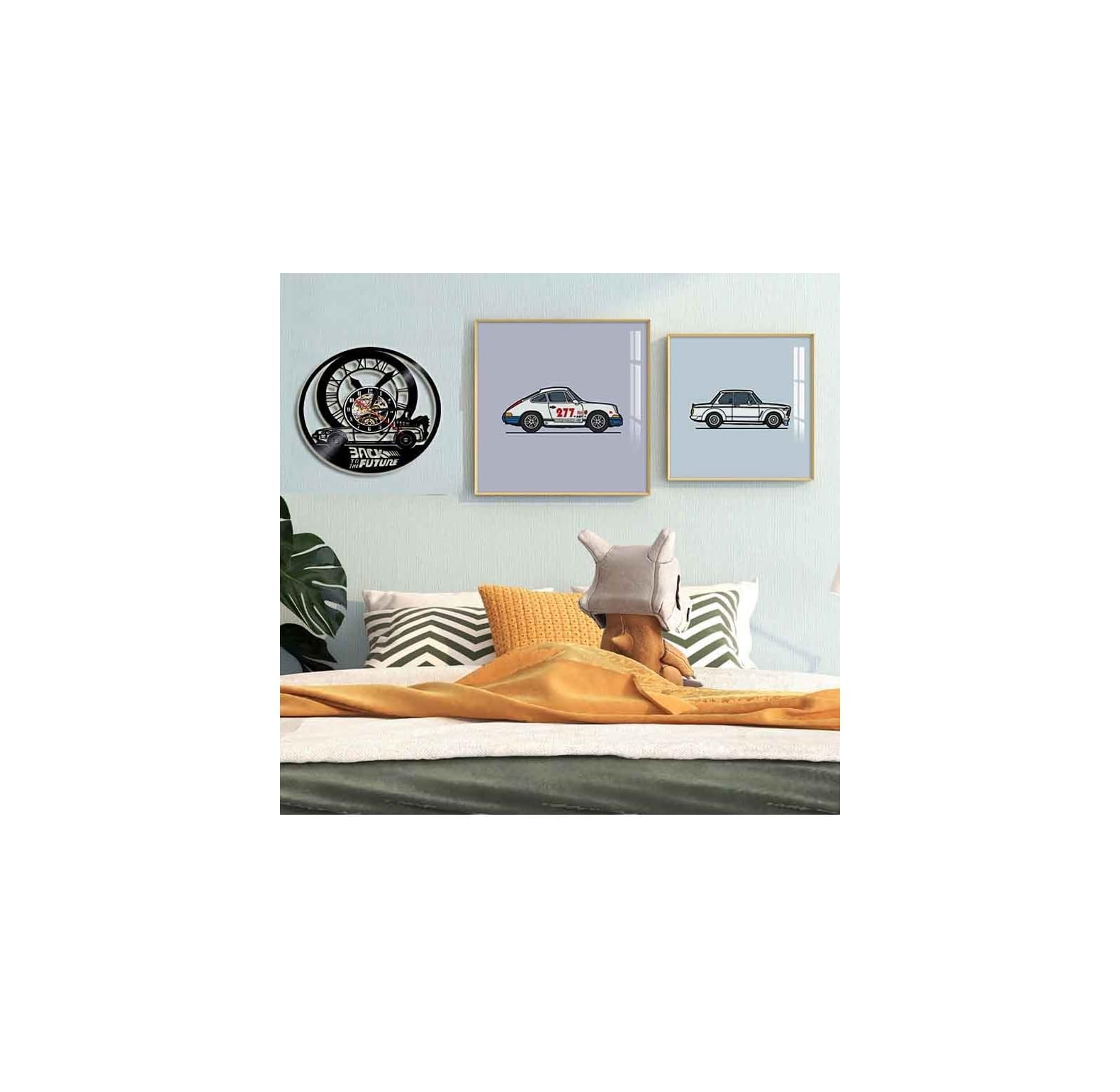 Wohnzimmer mit Bett, Kissen, Wanduhr mit Auto-Motiv und zwei gerahmten Bildern von Autos an der hellblauen Wand.