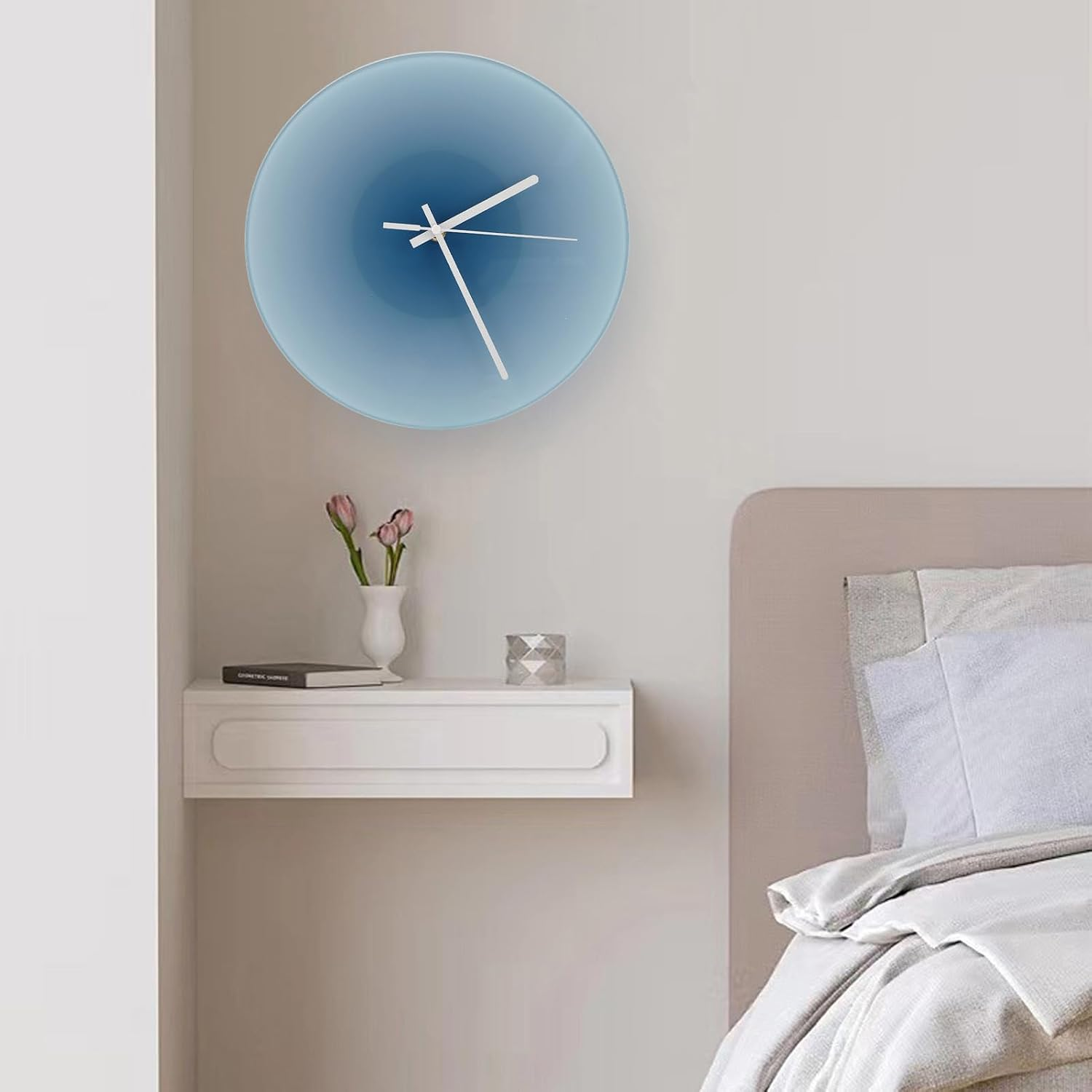 Eine blaue Wanduhr mit weißen Zeigern hängt über einem Nachttisch mit Blumen neben einem Bett.