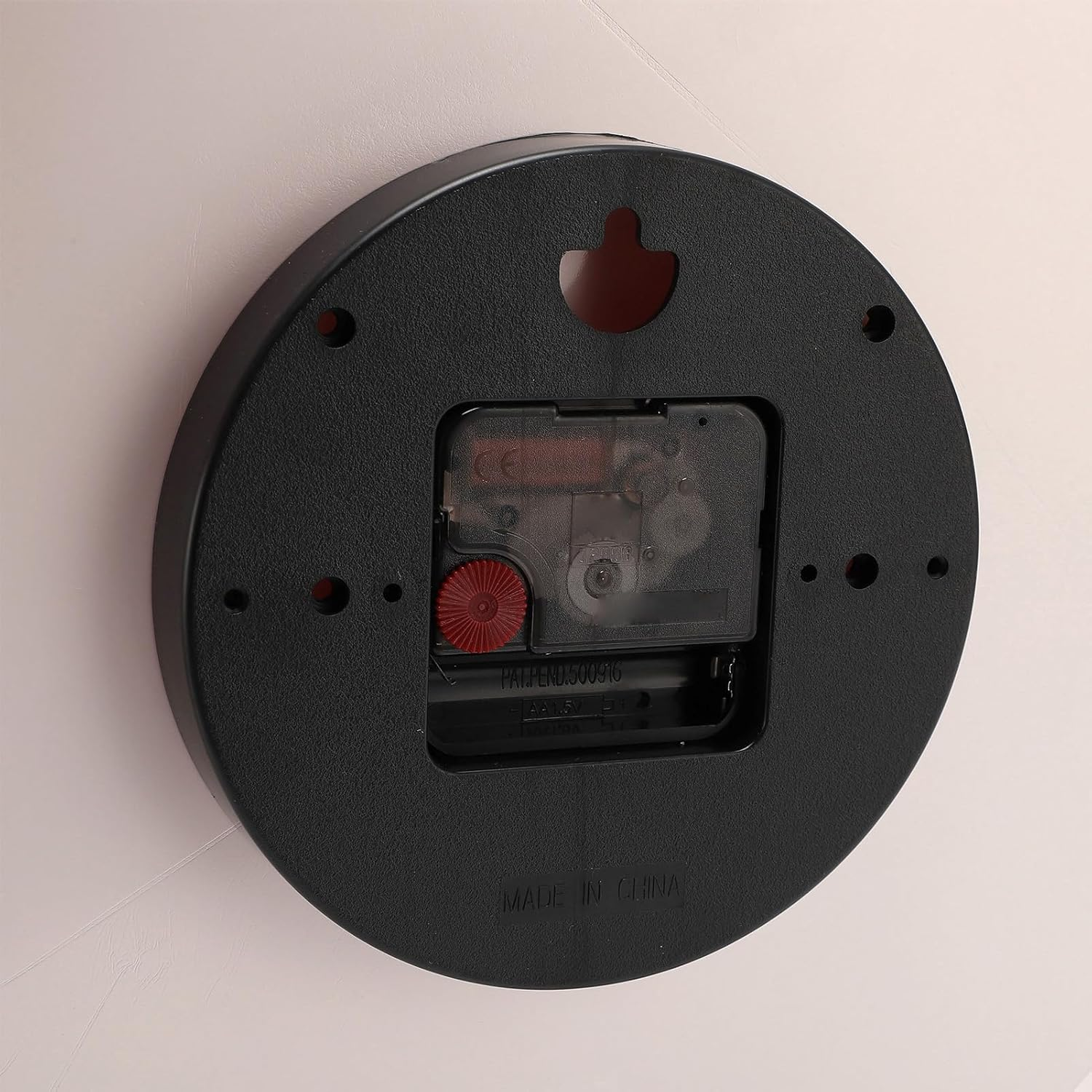Die Rückseite einer runden schwarzen Wanduhr mit einem zentralen Uhrwerk und einem roten Einstellrad.