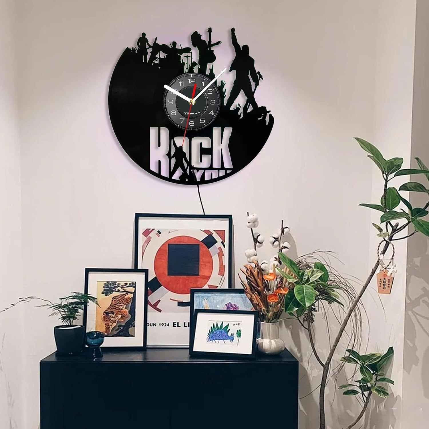 Eine schwarze Vinyluhr mit Rockband-Silhouette an einer Wand über gerahmten Bildern.