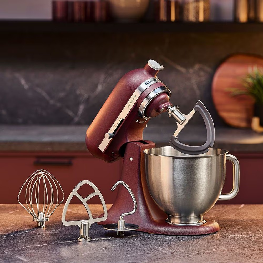Koyu tezgah üzerinde paslanmaz çelik kaseli ve üç aparatlı bordo renkli KitchenAid mutfak şefi.